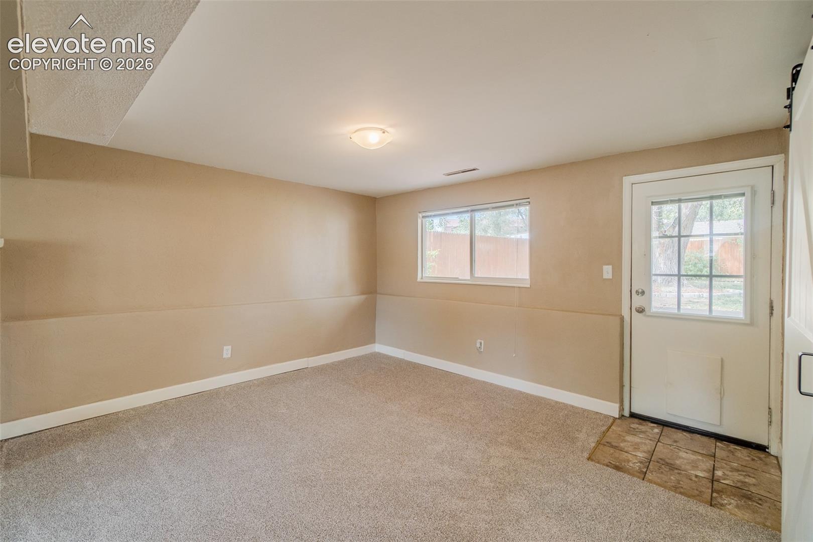 Neutral tone wall paint, carpeted flooring, flush mount ceiling light, exterior access door with window, and a barn door