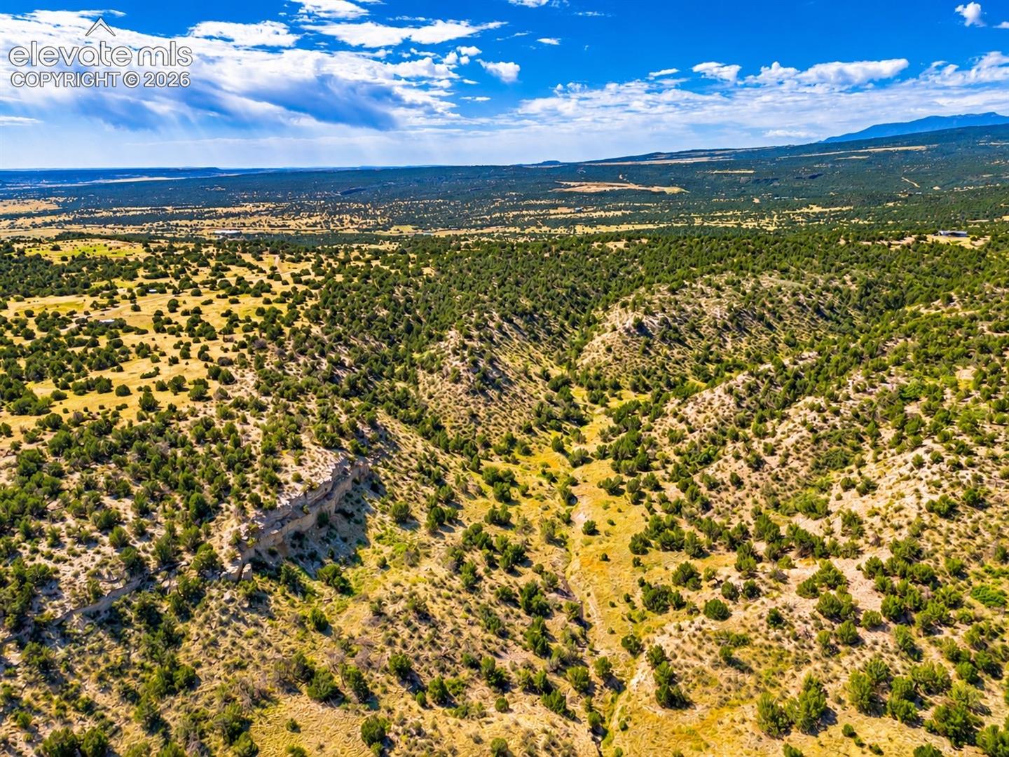 Elevated aerial view showcasing rugged rock formations, natural ravines, and open valleys with distant mountain ranges creating a beautiful backdrop.

