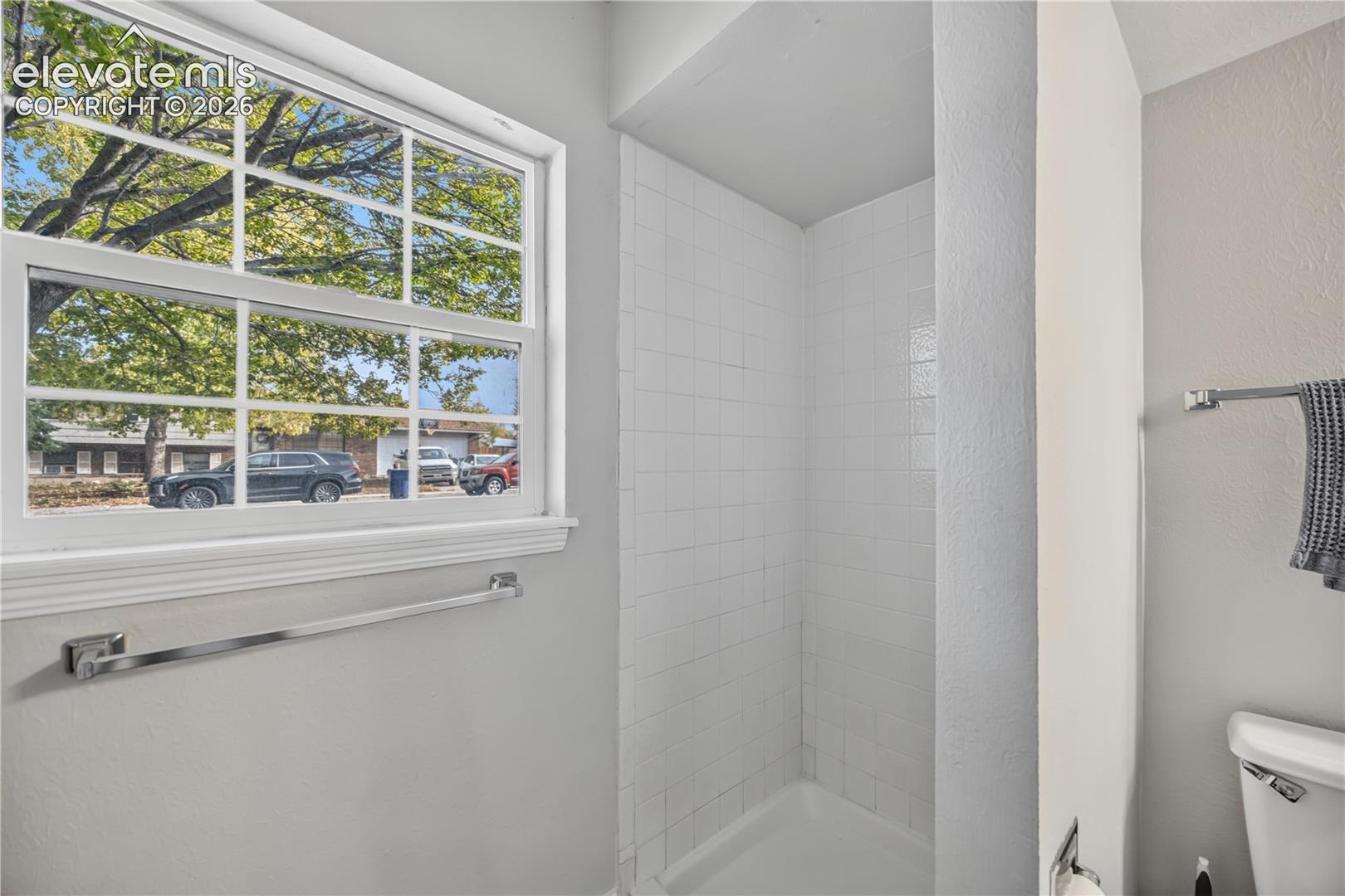 Shower stall with white subway tile surround, multi-pane window with exterior natural light, and chrome hardware throughout