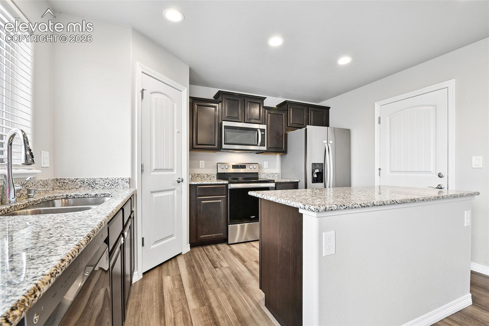 Kitchen featuring dark cabinetry, stone-finish countertops, stainless steel appliances, a center island, and wood-finish flooring