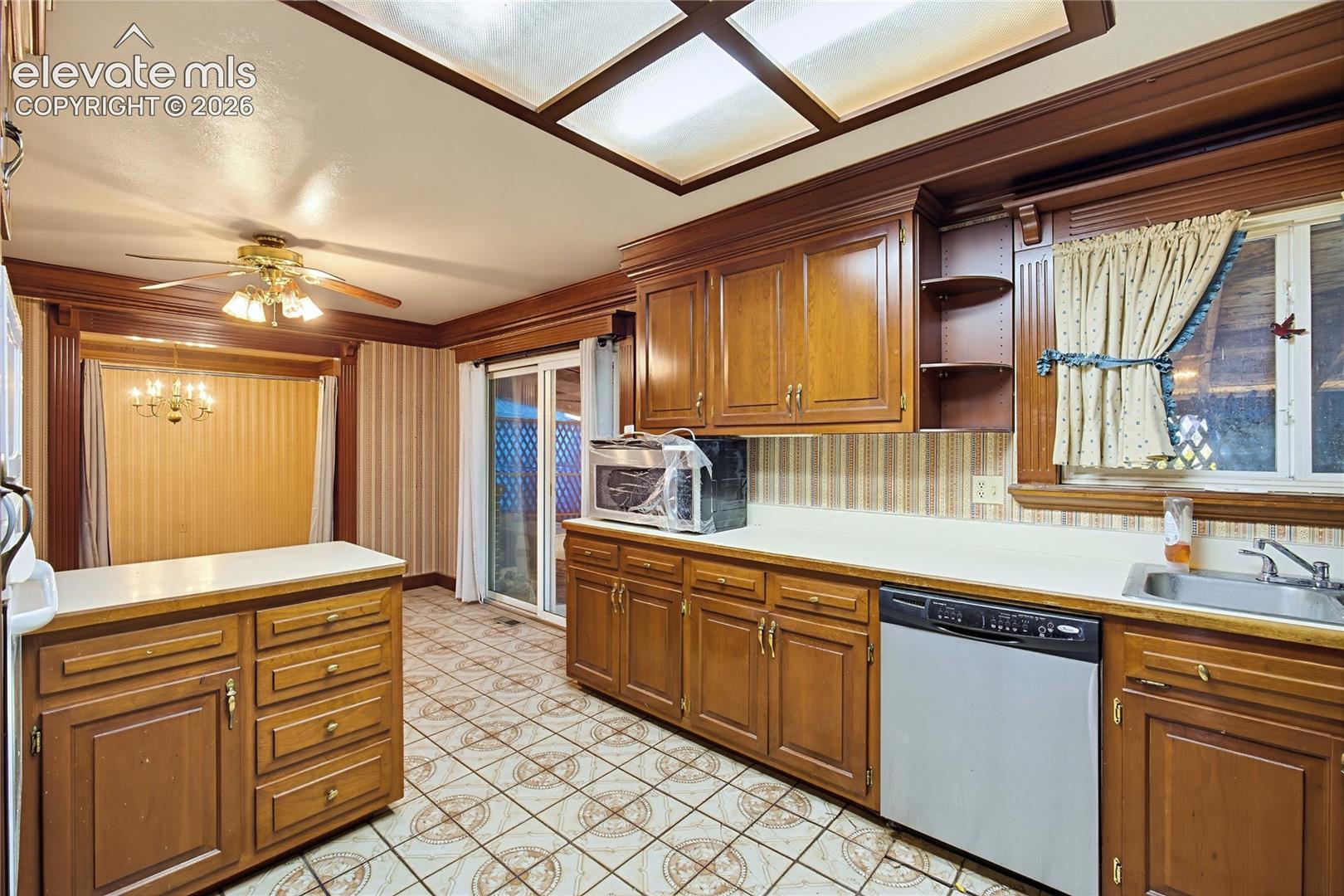 Kitchen featuring wood-finish cabinetry, patterned flooring, a ceiling fan, a window over the sink, and a sliding glass door