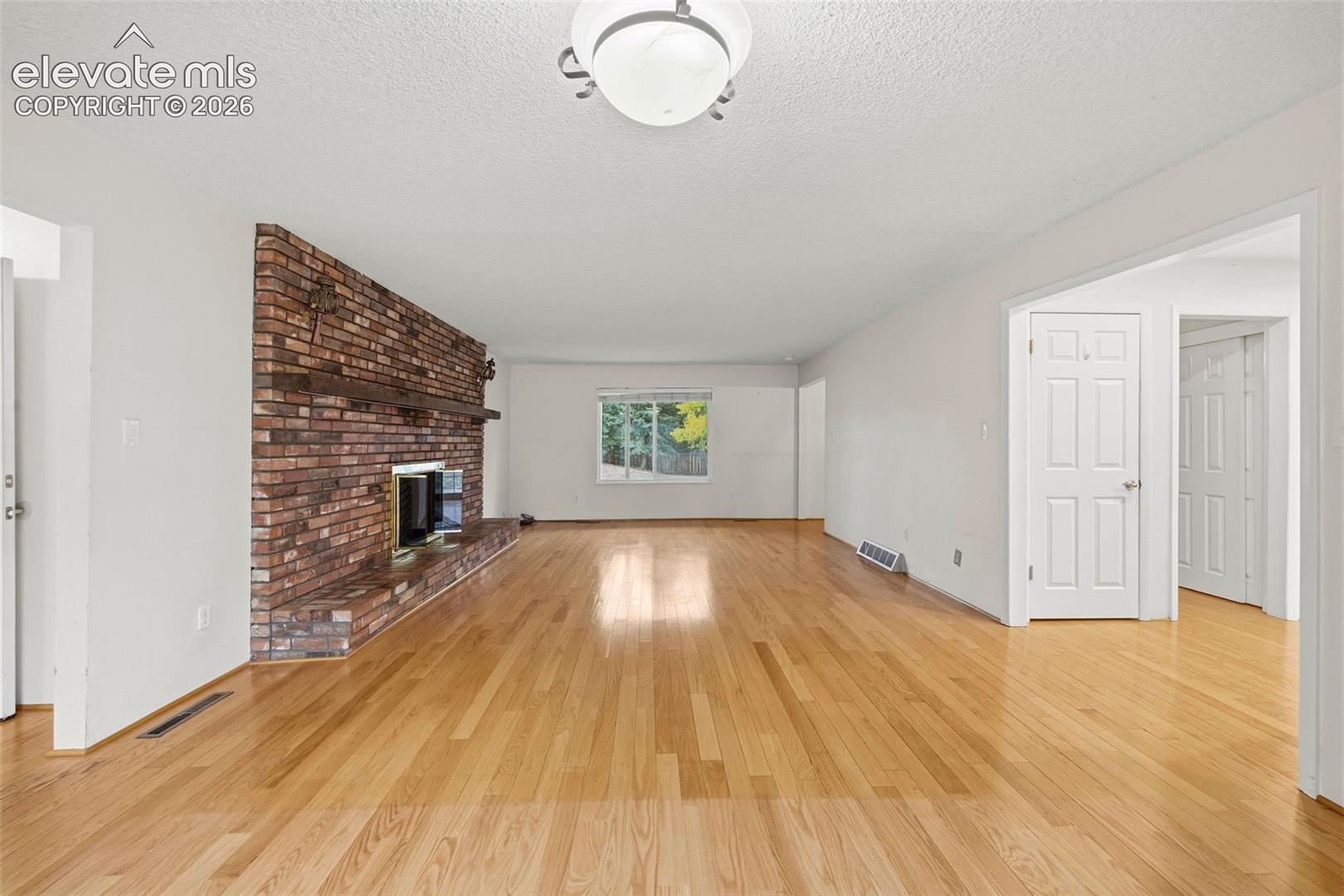 Living area featuring wood-finish flooring, a floor-to-ceiling brick fireplace with a wood mantel, a raised brick hearth, and paneled doors
