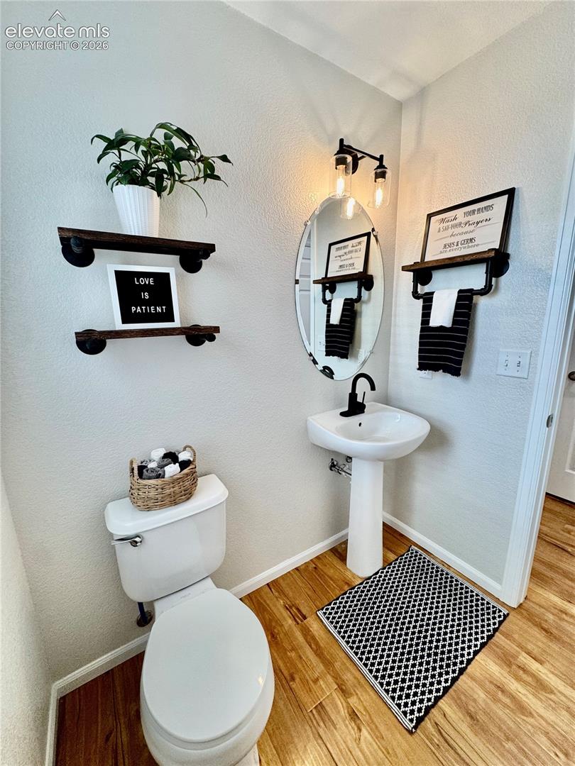 Powder room featuring wood-finish flooring, a white pedestal sink with a matte black faucet, and an oval mirror