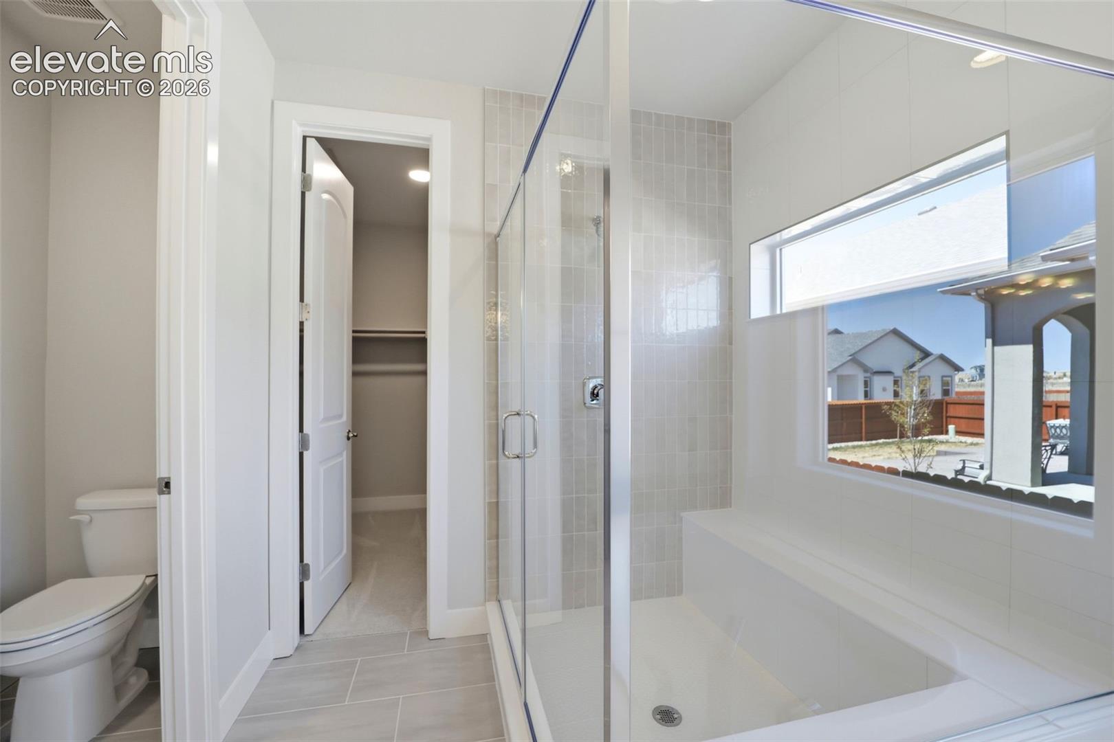 Walk-in shower with a glass enclosure, tiled surround, and integrated bench, accompanied by large-format tile flooring and an attached reach-in closet