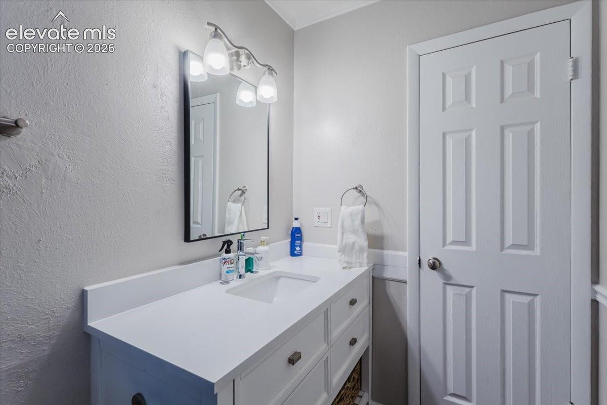 White vanity with integrated sink, brushed nickel lighting fixture, framed mirror, and a paneled door