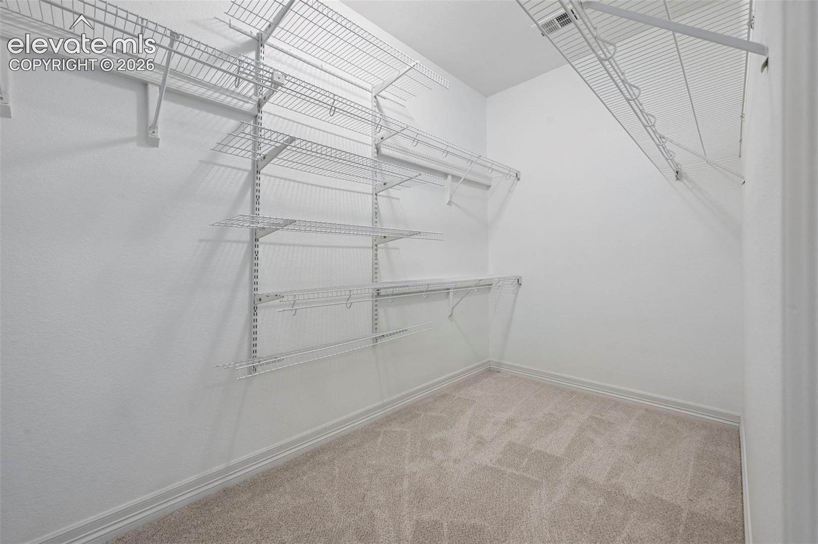 Walk-in closet featuring white wire shelving, white wire racks, and light-toned patterned carpeting