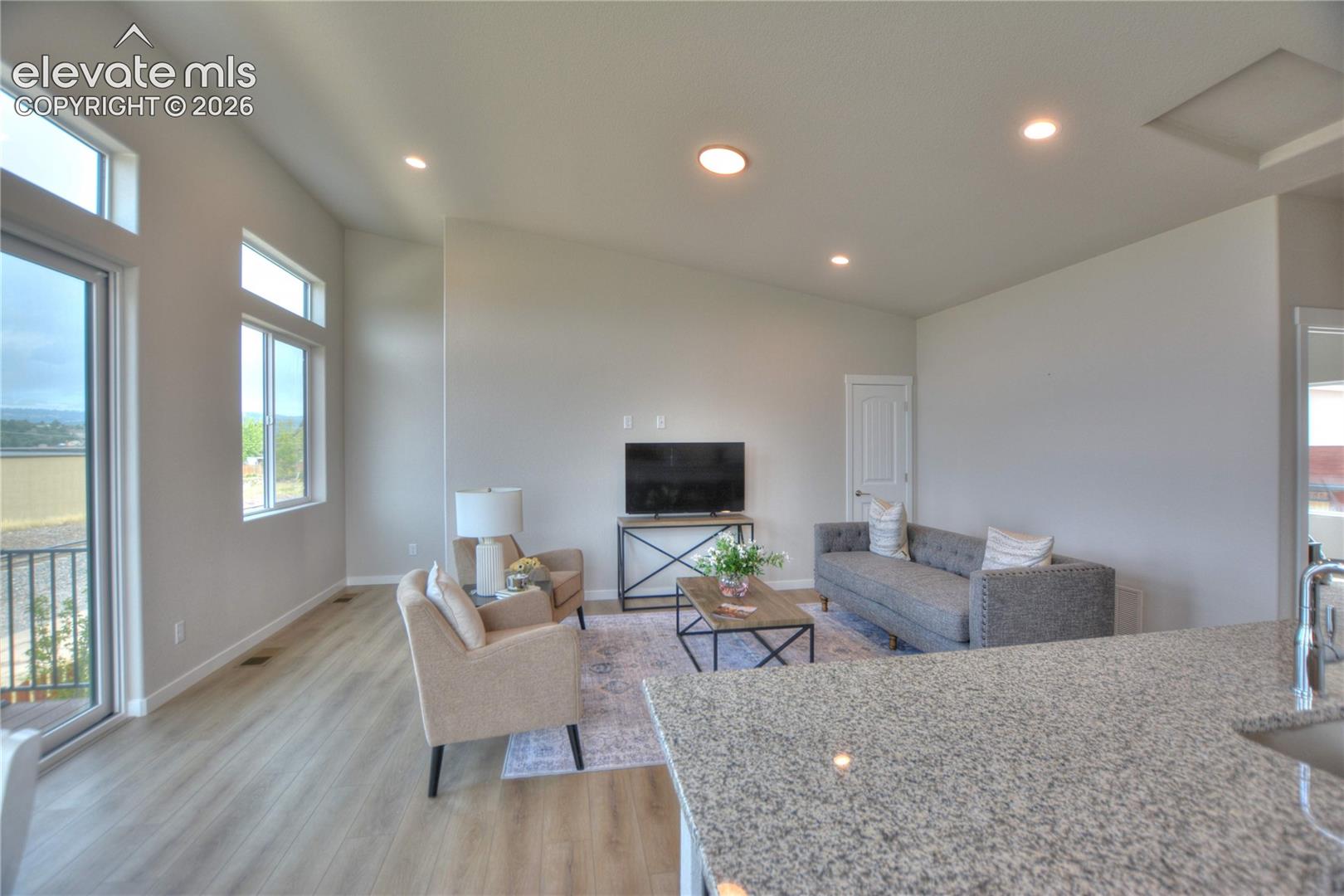 Open-concept living area showcasing wood-finish flooring throughout, recessed ceiling lighting, and expansive windows with natural light