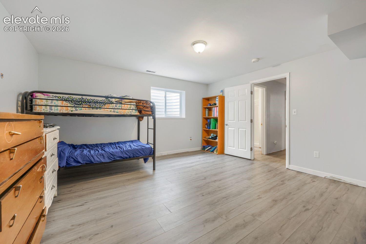 Light wood-finish flooring, white walls, and a window with horizontal blinds