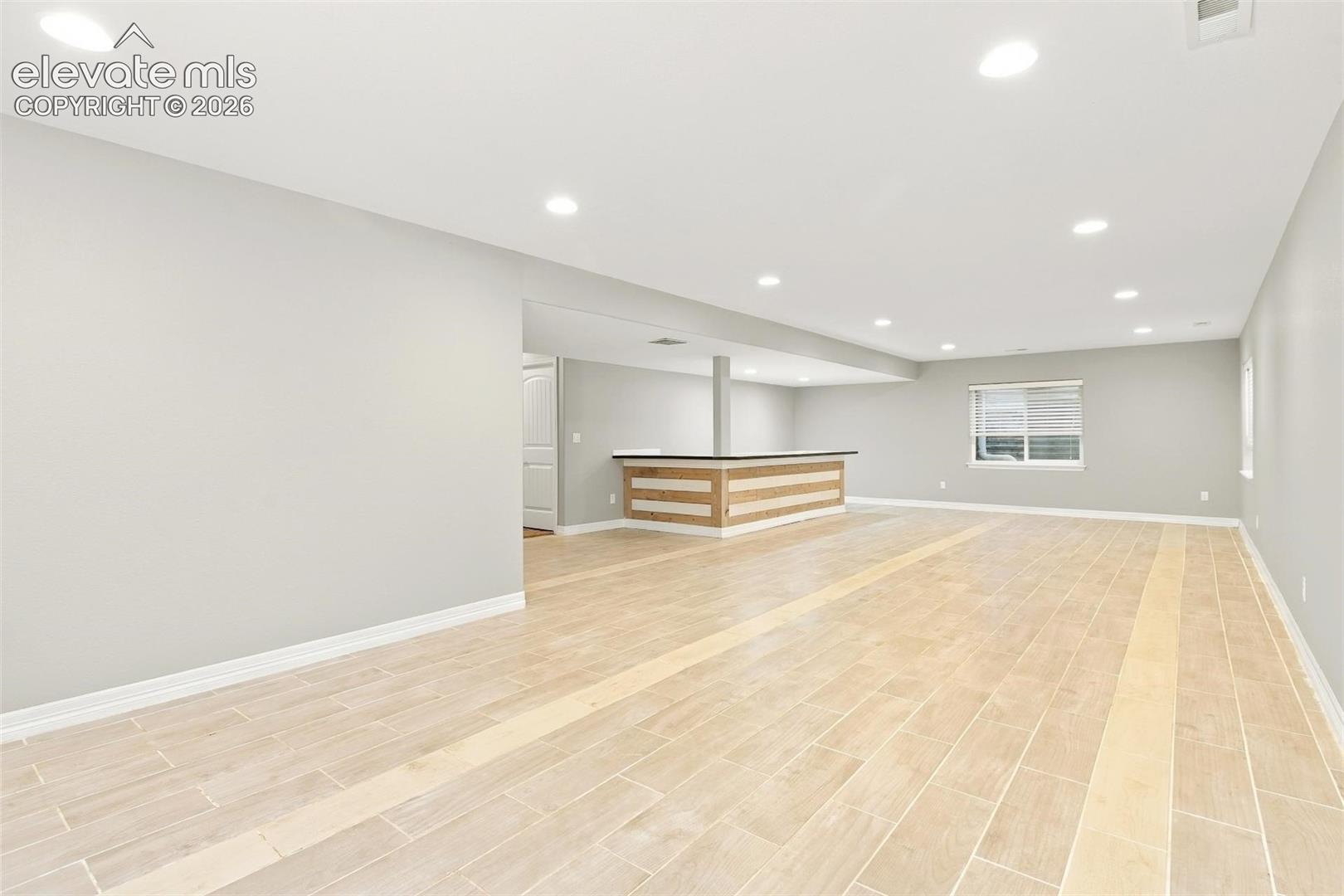 Open-concept interior featuring light wood-finish flooring, recessed lighting, and a built-in bar with wood-paneled trim