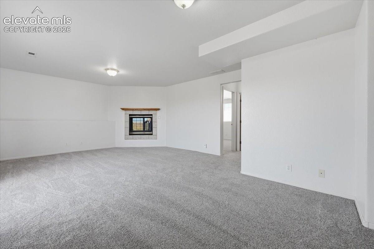 Spacious room with light gray carpeting, a built-in fireplace featuring a stone surround and wood mantle, and white walls