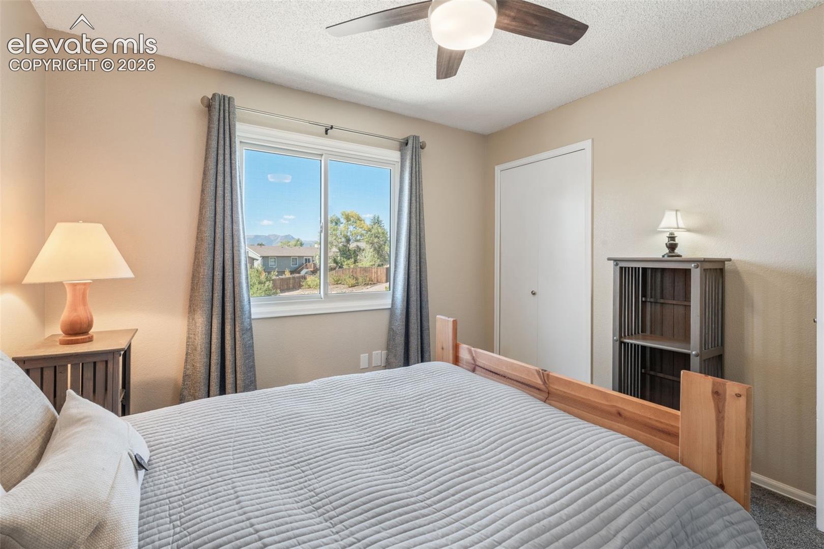 Bedroom featuring a textured ceiling, ceiling fan with light fixture, sliding glass window, and a closet with a solid-core door