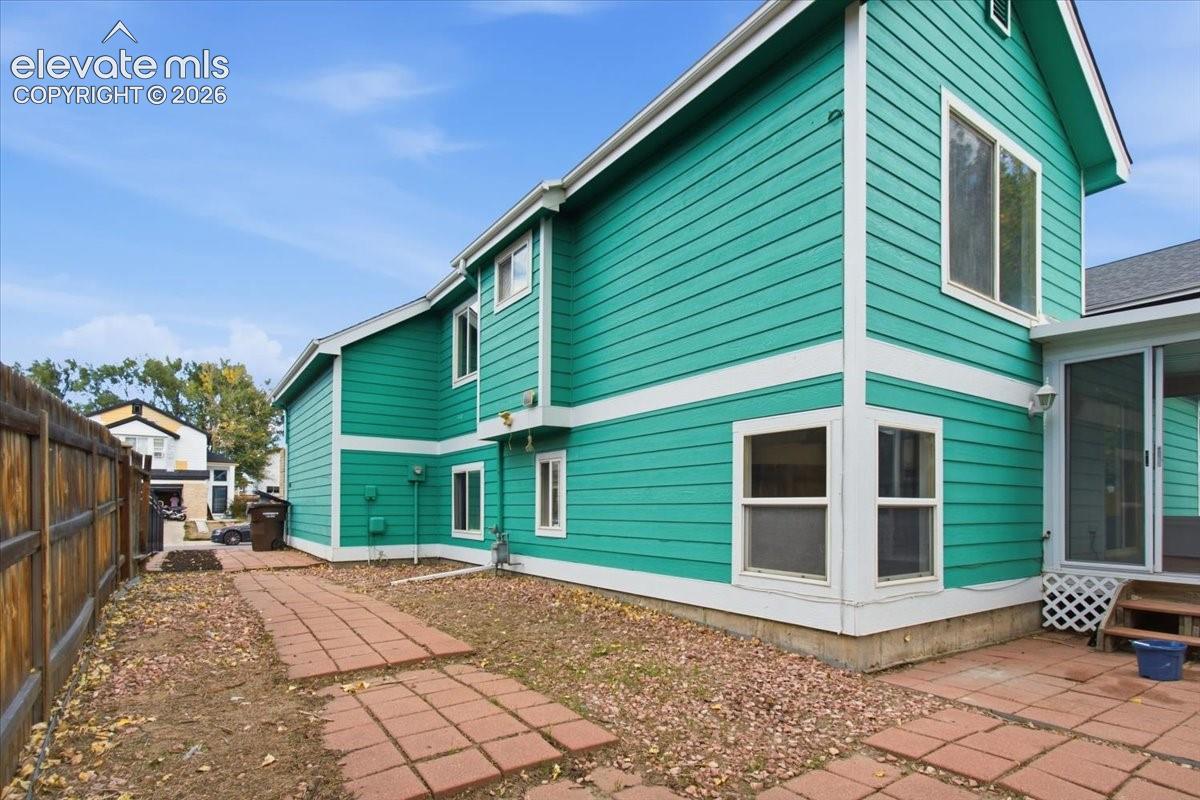 Two-story exterior with horizontal siding, a stone-paver patio, a wood-slat privacy fence, and multiple window placements