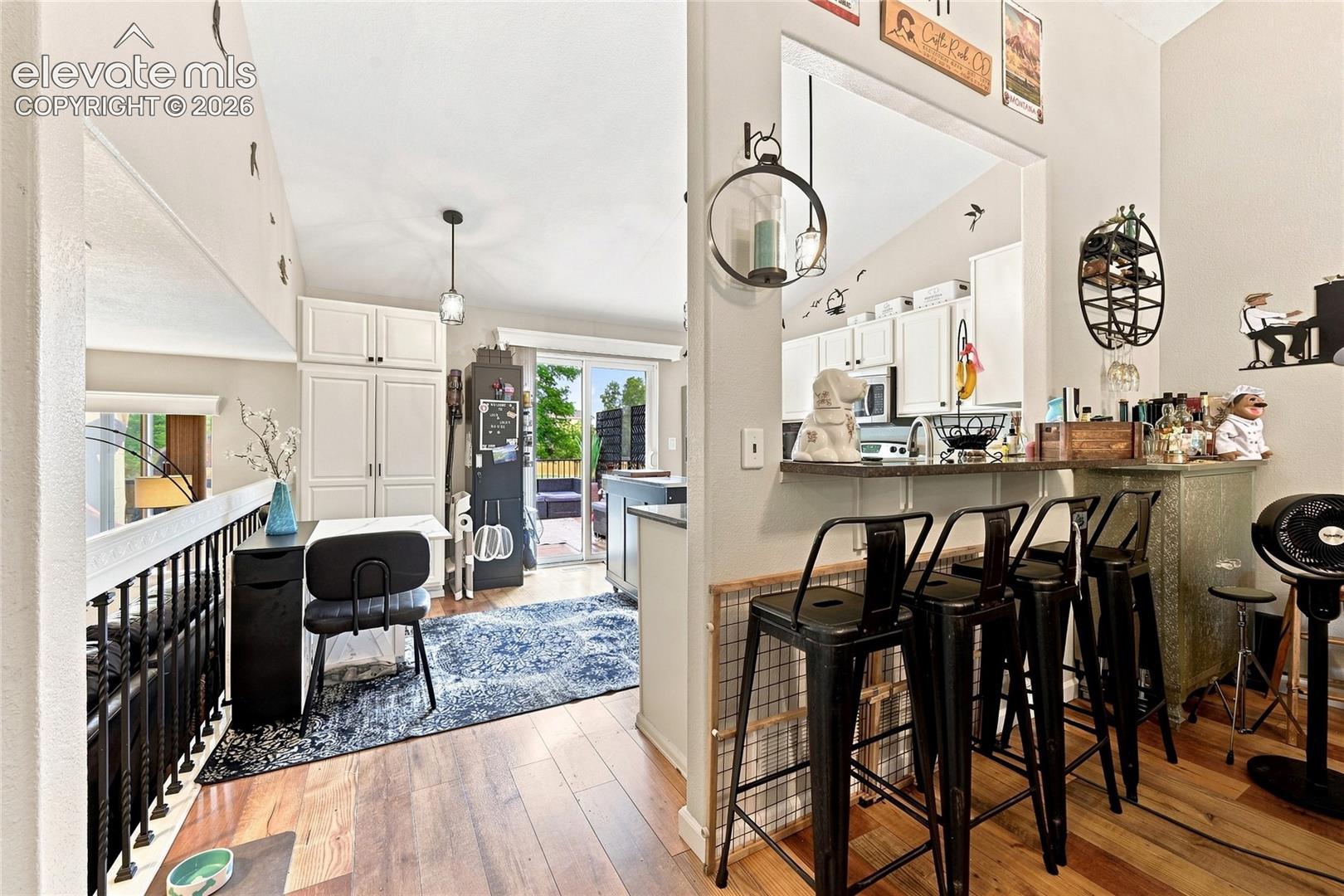 Kitchen featuring white cabinetry, a breakfast bar with stone-finish countertop, wood-finish flooring, and a sliding glass door
