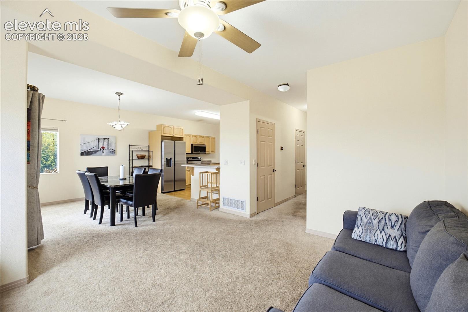 Open-concept living space with a ceiling fan, dining area with pendant lighting, and a kitchen featuring stainless steel appliances and light wood cabinetry