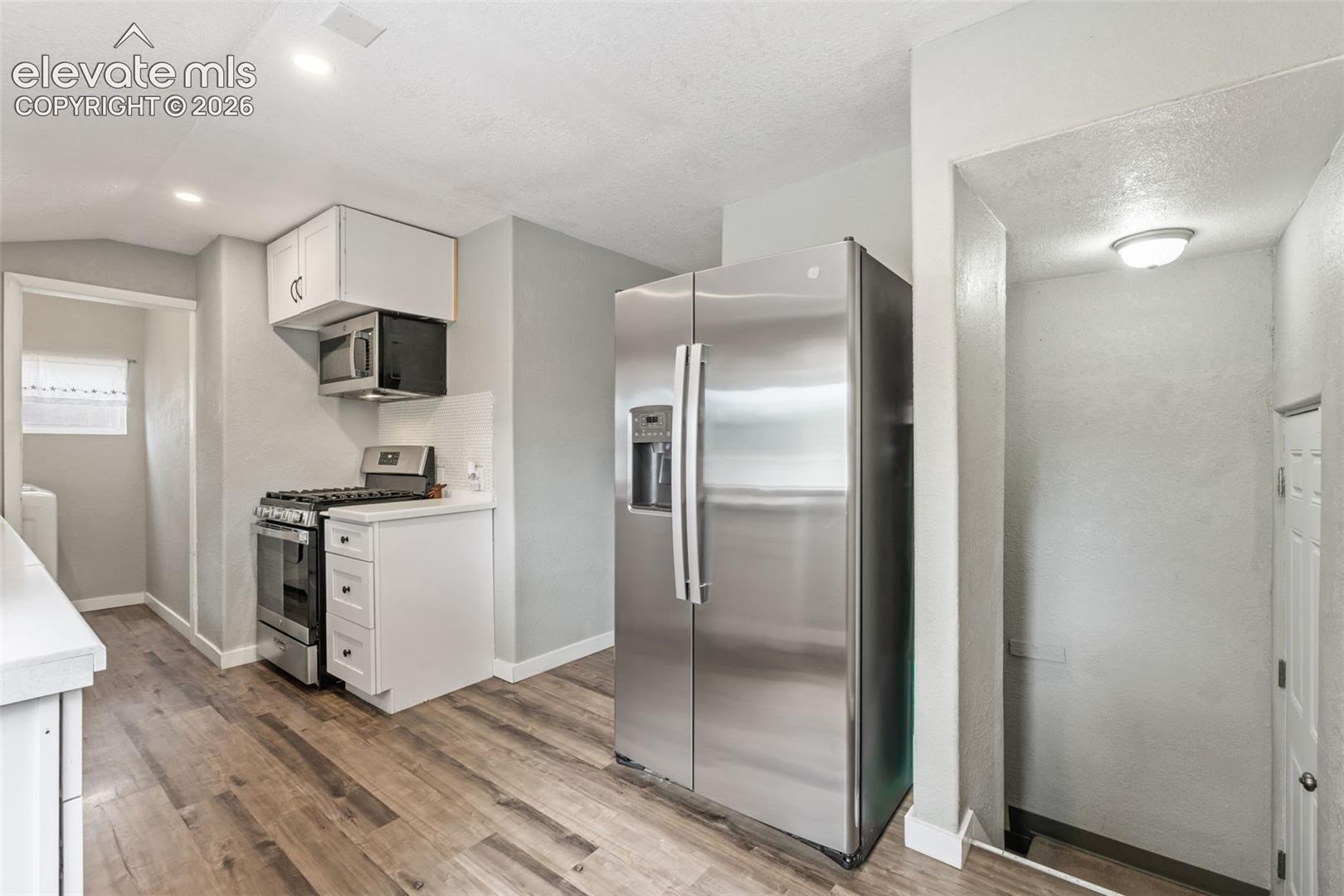 Kitchen featuring wood-finish flooring, white cabinetry, and stainless steel appliances including a side-by-side refrigerator, gas range, and built-in microwave