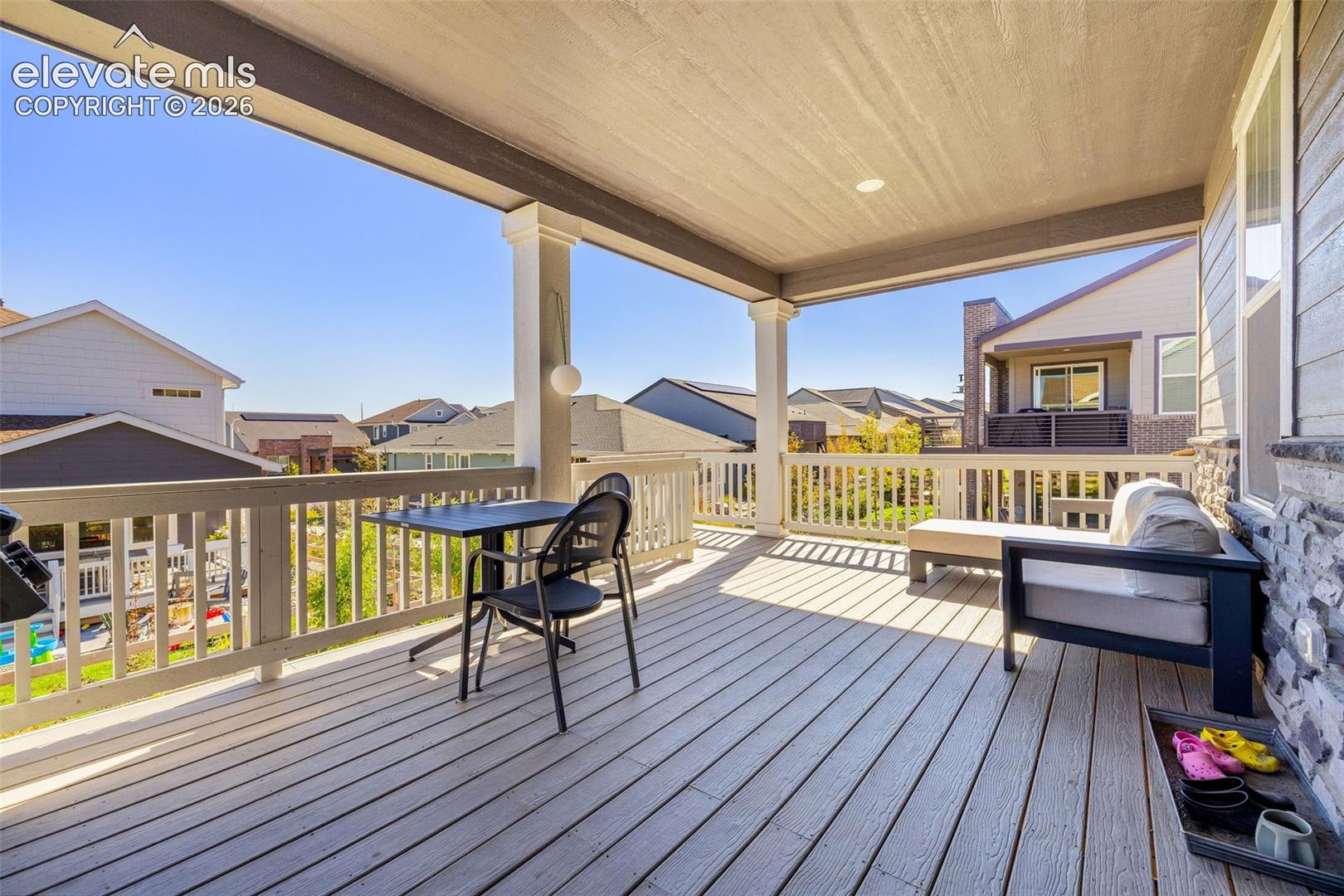 Covered outdoor deck with light wood-finish flooring, white railing, and stone siding accent