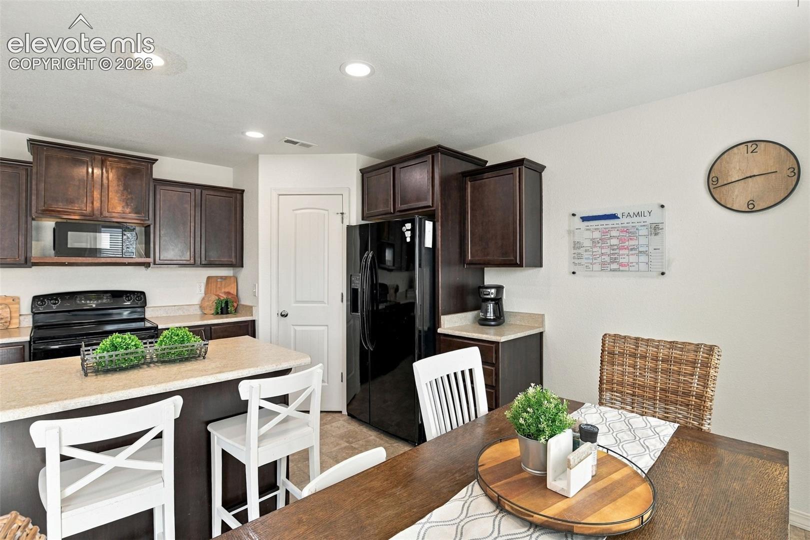 Kitchen featuring dark wood-finish cabinetry, black appliances, light-toned countertops, a breakfast bar, and recessed lighting