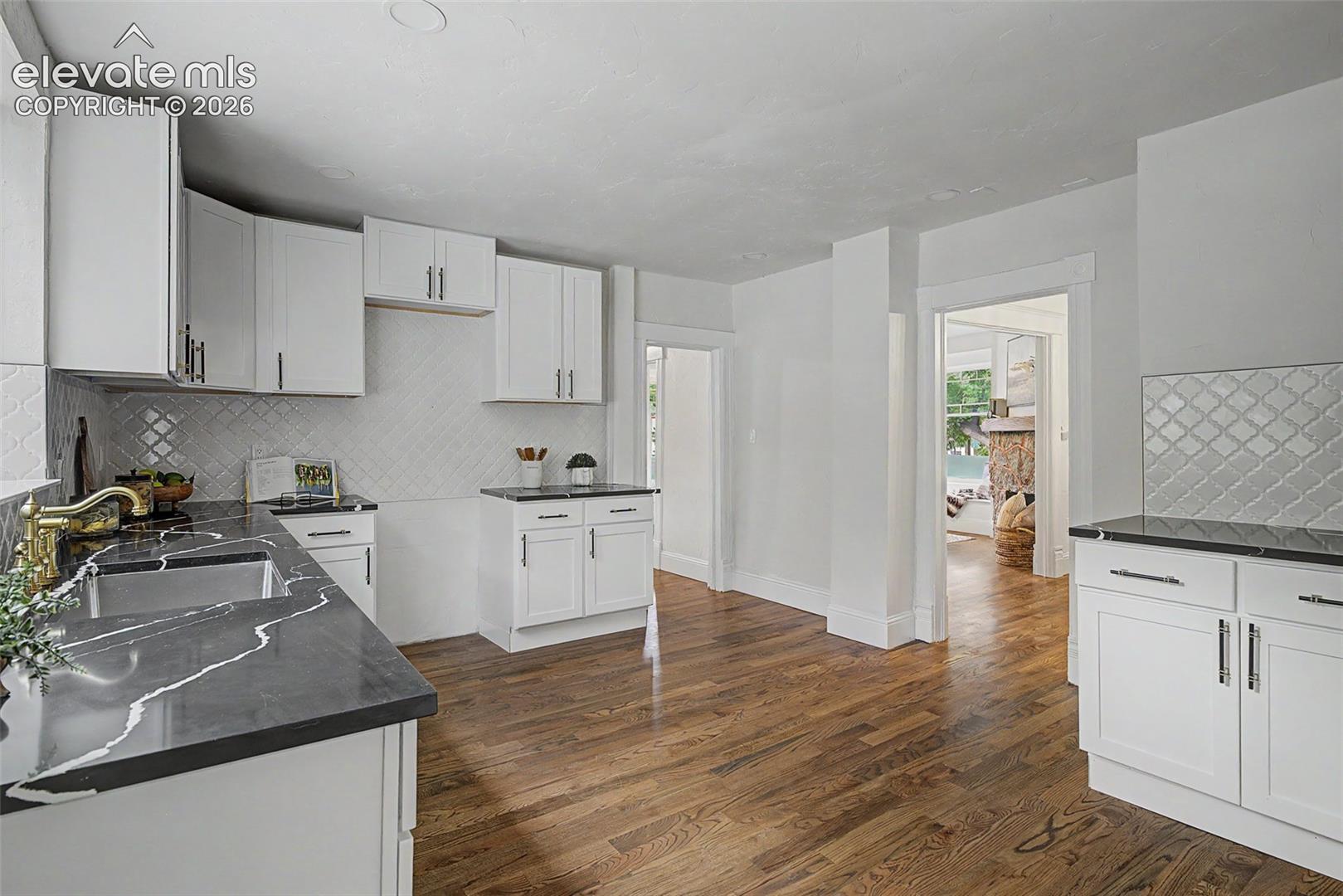 Spacious kitchen featuring white cabinetry, dark countertops with distinctive veining, a patterned tile backsplash, and wood-finish flooring