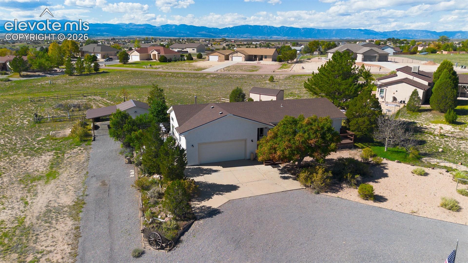 Single-story residence featuring a multi-car garage, expansive graveled driveway, detached storage structure, and mountain range backdrop