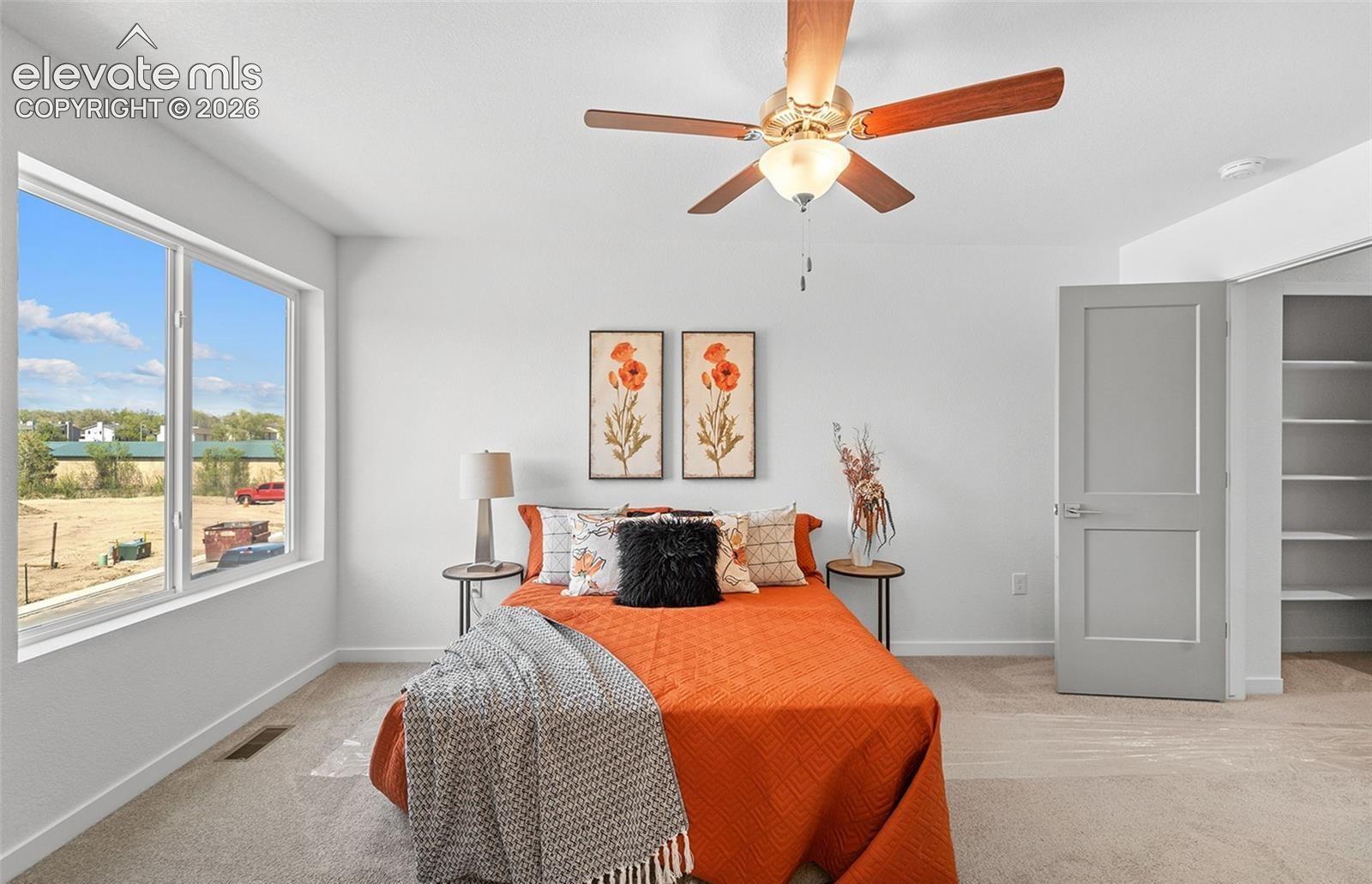 Neutral-toned carpeting, oversized window, ceiling fan with light fixture, gray interior door, and built-in shelving unit