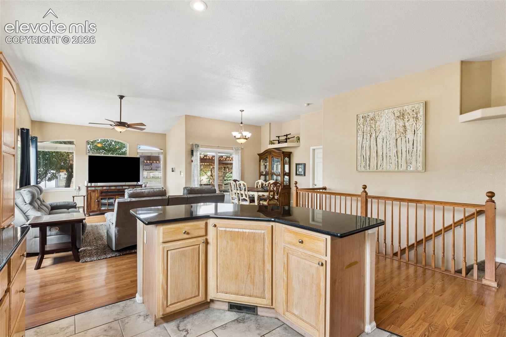 Kitchen island with stone countertop, wood-finish flooring, and wooden staircase railing