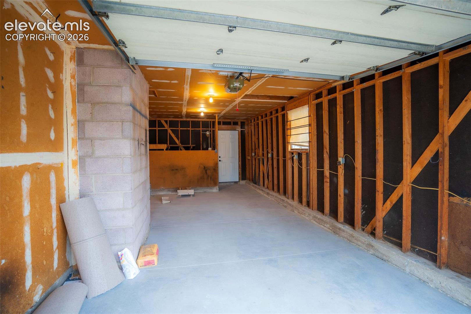 Unfinished garage space featuring a concrete floor, exposed structural wall framing, block masonry pillar, and a single pedestrian entry door