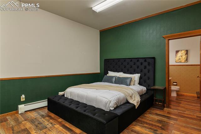 Bedroom featuring baseboard heating, dark wood finished floors, wallpapered walls, and an accent wall