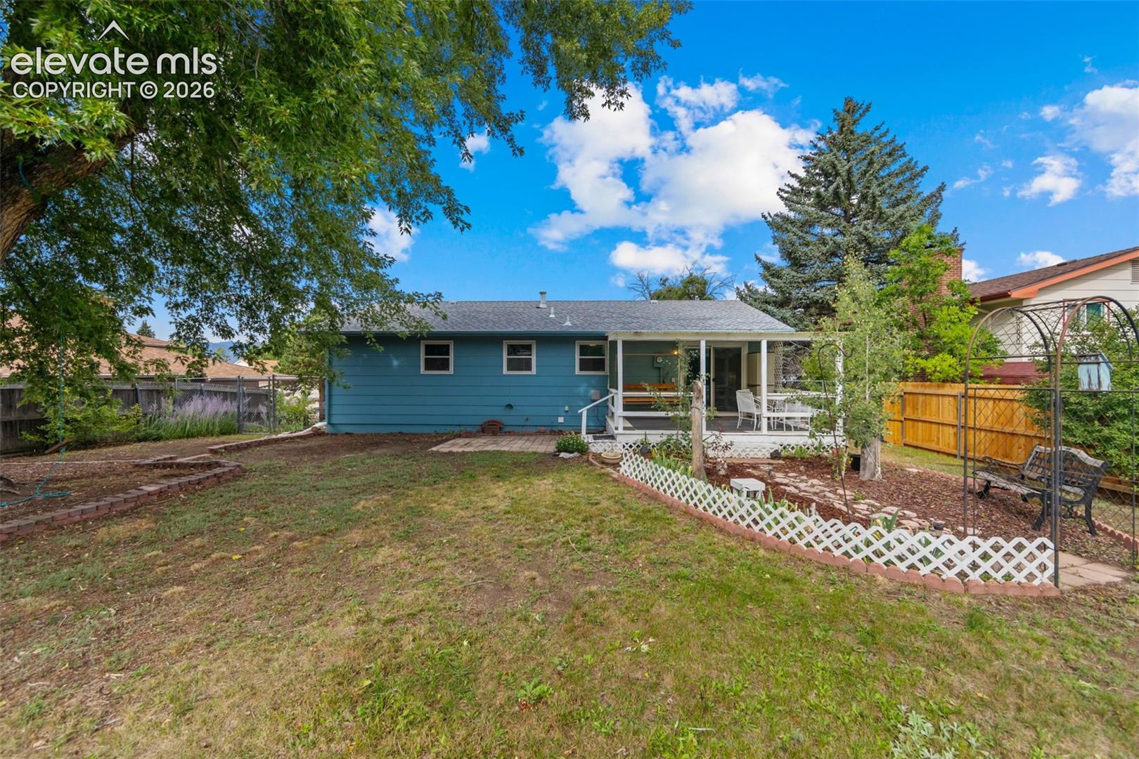Expansive backyard with a covered deck, tiered landscaping beds, mature trees, and a privacy fence
