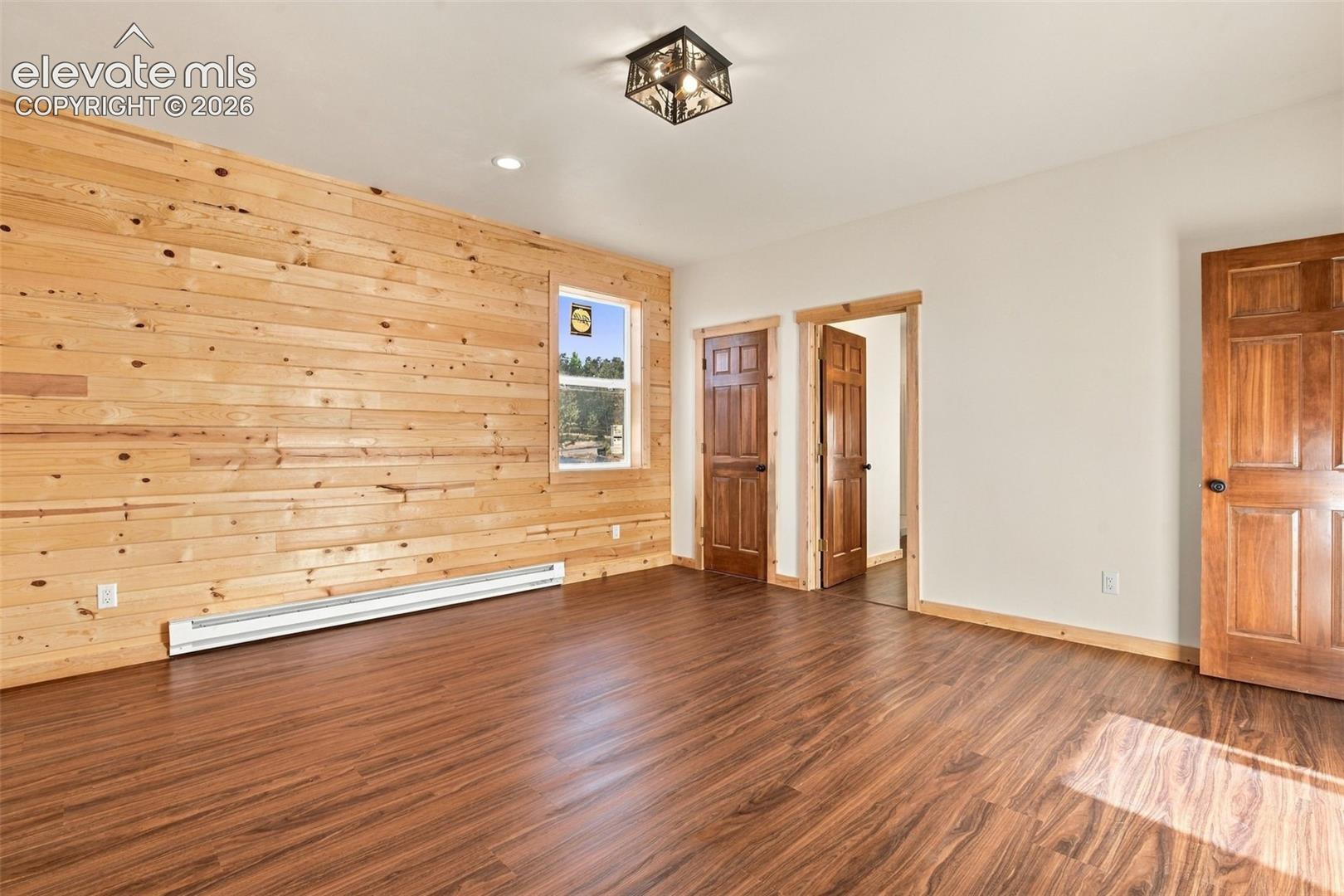 Room featuring horizontal wood-plank wall paneling, wood-finish flooring, solid wood-paneled interior doors, and a decorative flush-mount ceiling fixture