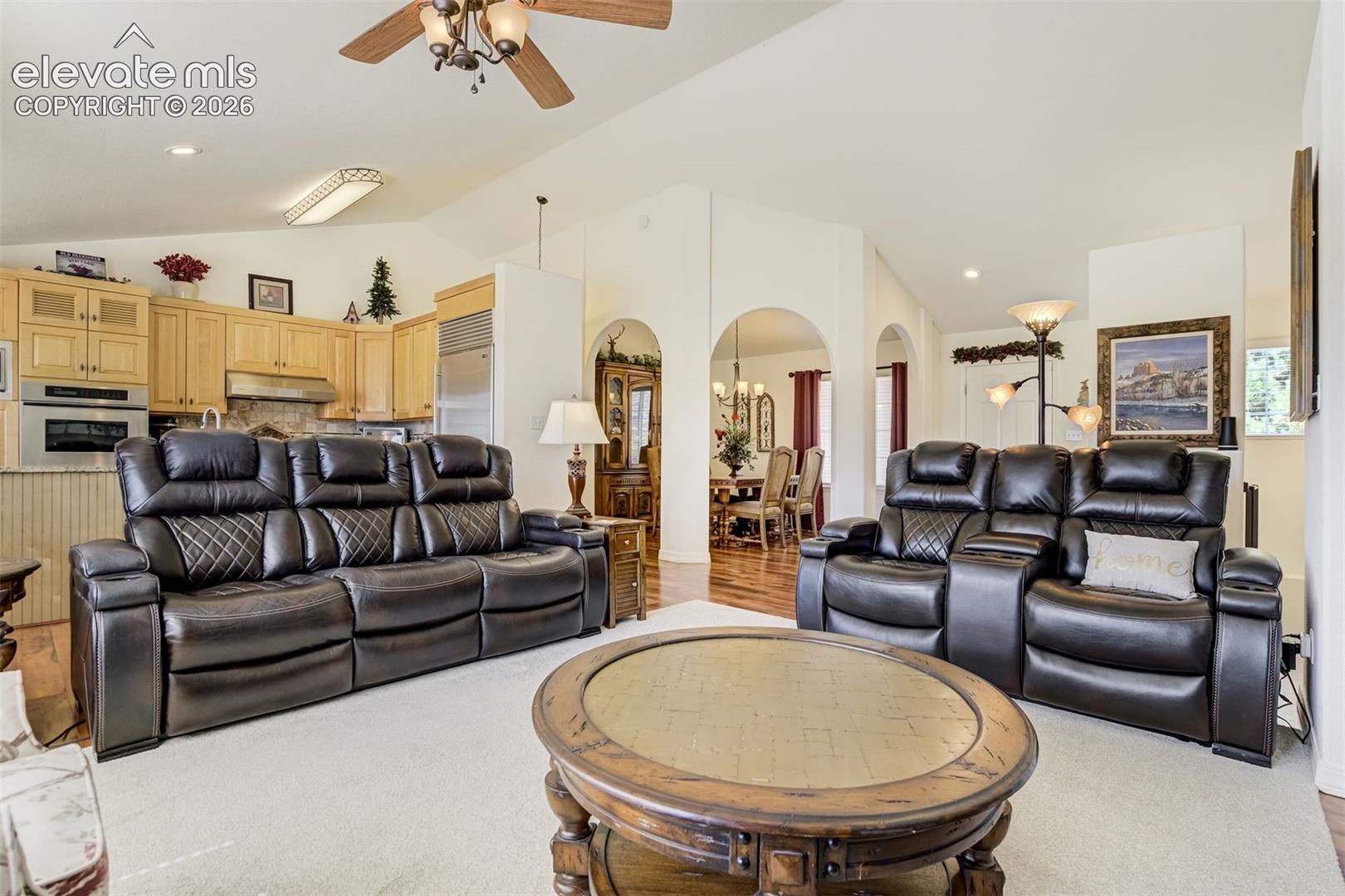 Open-concept living space featuring vaulted ceilings, architectural archways, built-in light-wood cabinetry, stainless steel appliances, and recessed lighting