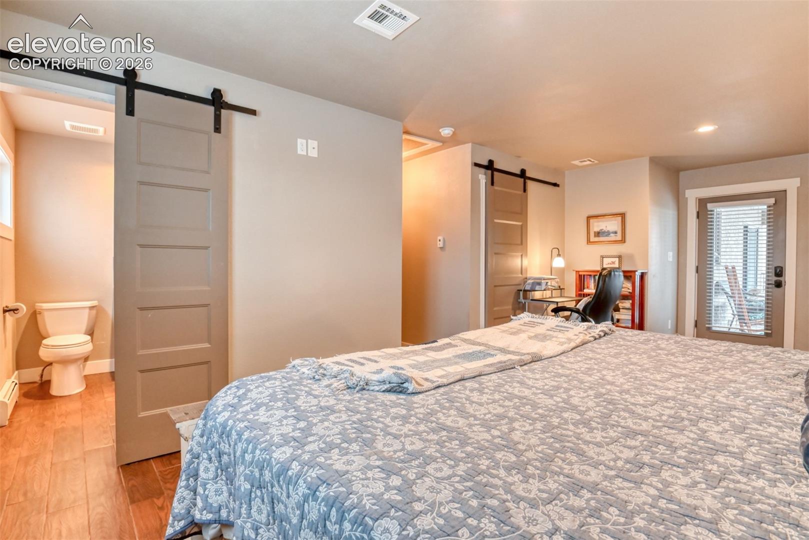 Bedroom featuring a barn door, multiple windows, light wood-style floors, an office area, and recessed lighting