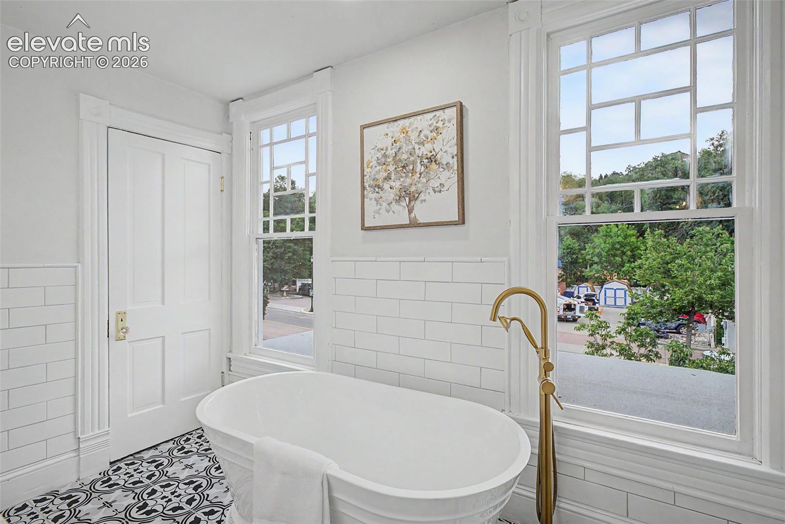 Freestanding soaking tub with a floor-mounted brass faucet, complemented by black and white patterned tile flooring