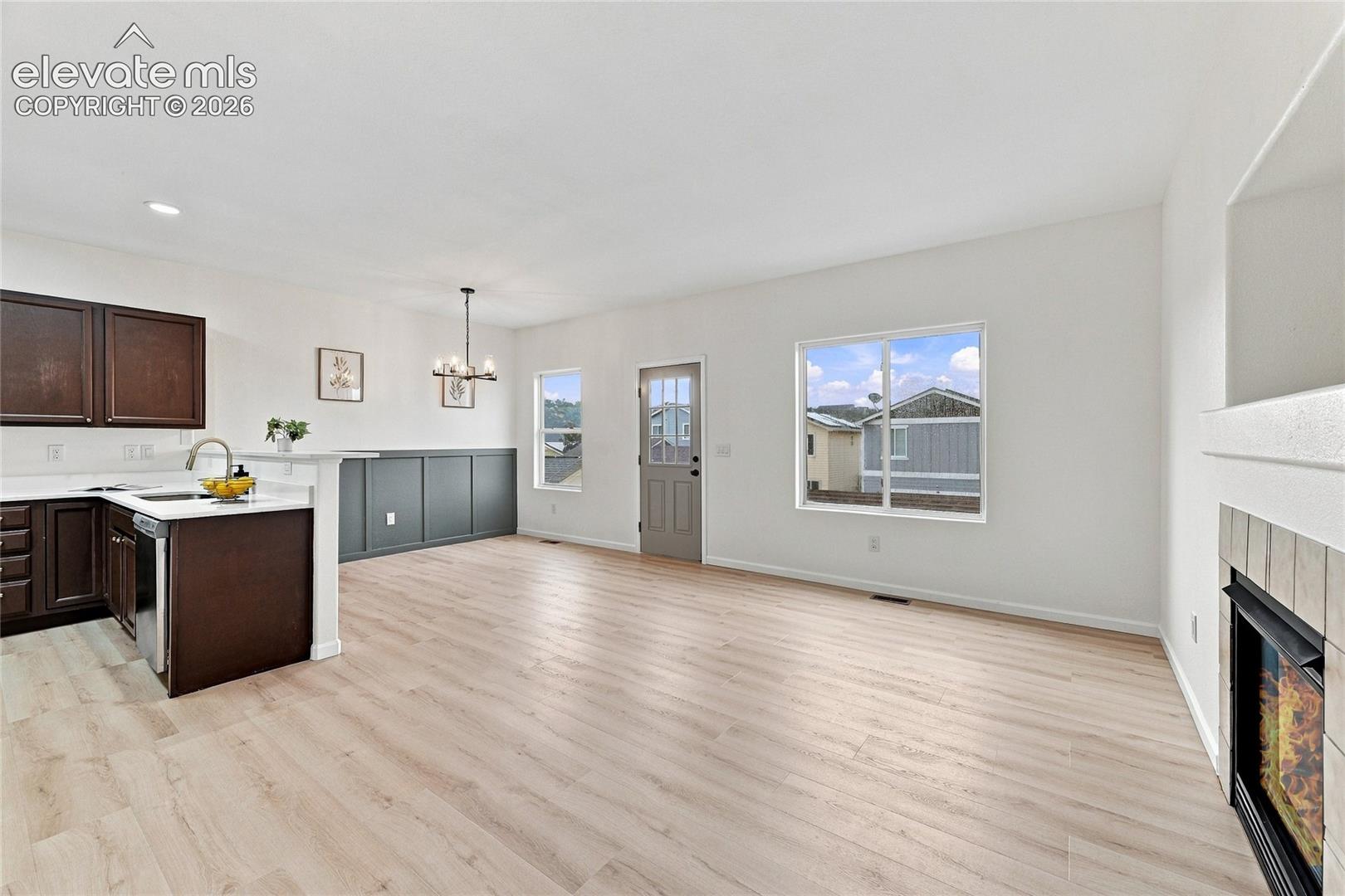 Open-concept interior featuring light wood-finish flooring, dark wood cabinetry, a decorative wall paneling accent, and a built-in tiled fireplace