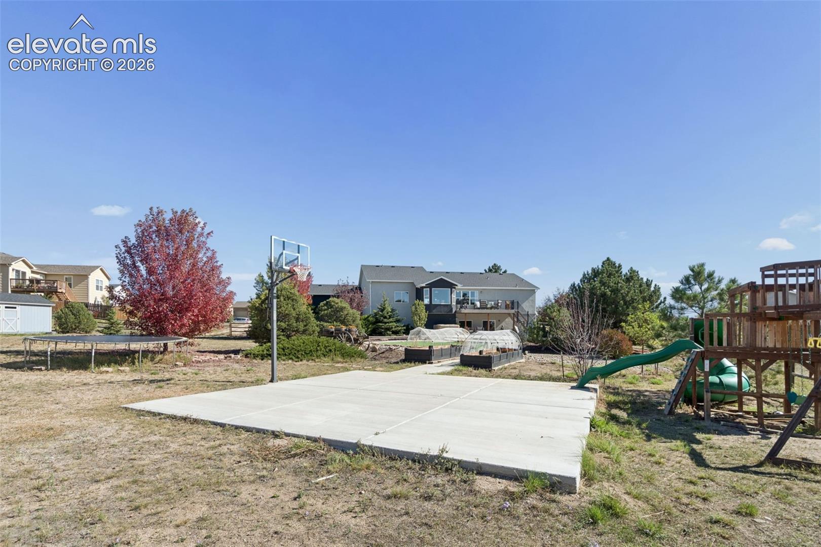 Expansive backyard featuring a concrete sports court with a basketball hoop, raised garden beds, and mature landscaping