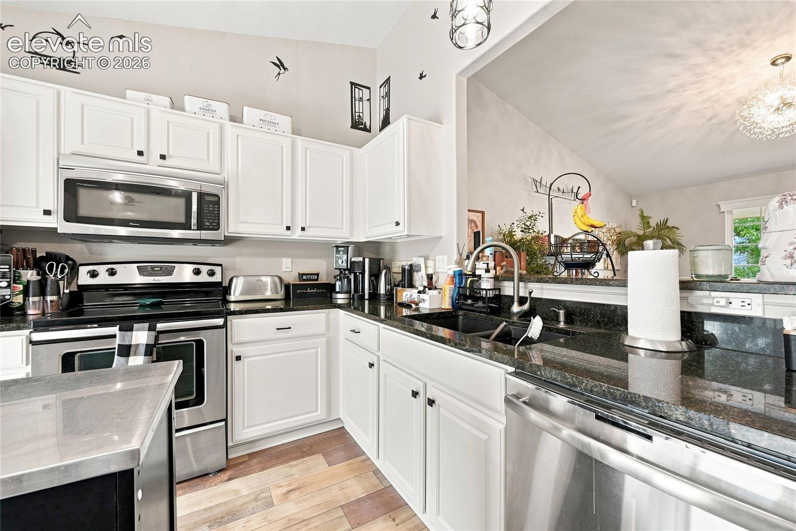 Kitchen featuring white cabinetry, dark stone countertops, stainless steel appliances, and wood-finish flooring