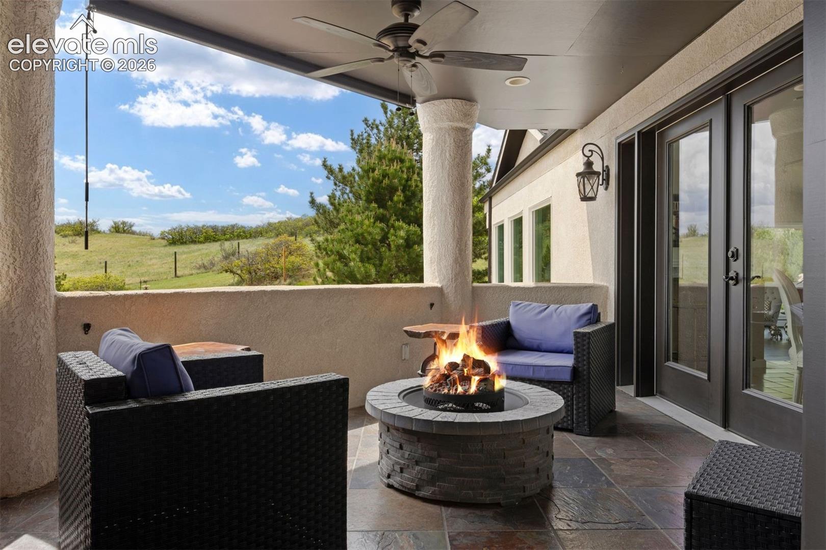 Covered deck located off the kitchen and living areas, with stone columns, pull-down sun shade, ceiling fan, slate tile flooring, and rolling hill views.
