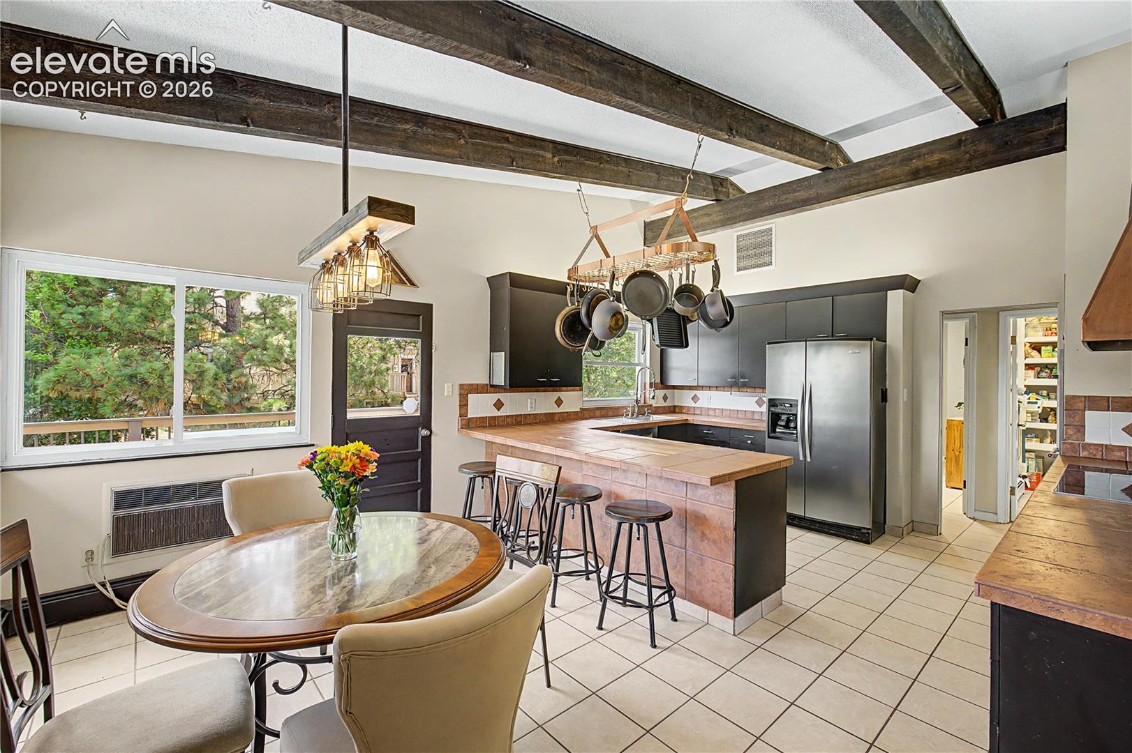 A sunlit breakfast nook, framed by corner windows and exposed wood ceiling beams, offers a front-row seat to the mature pines just outside.