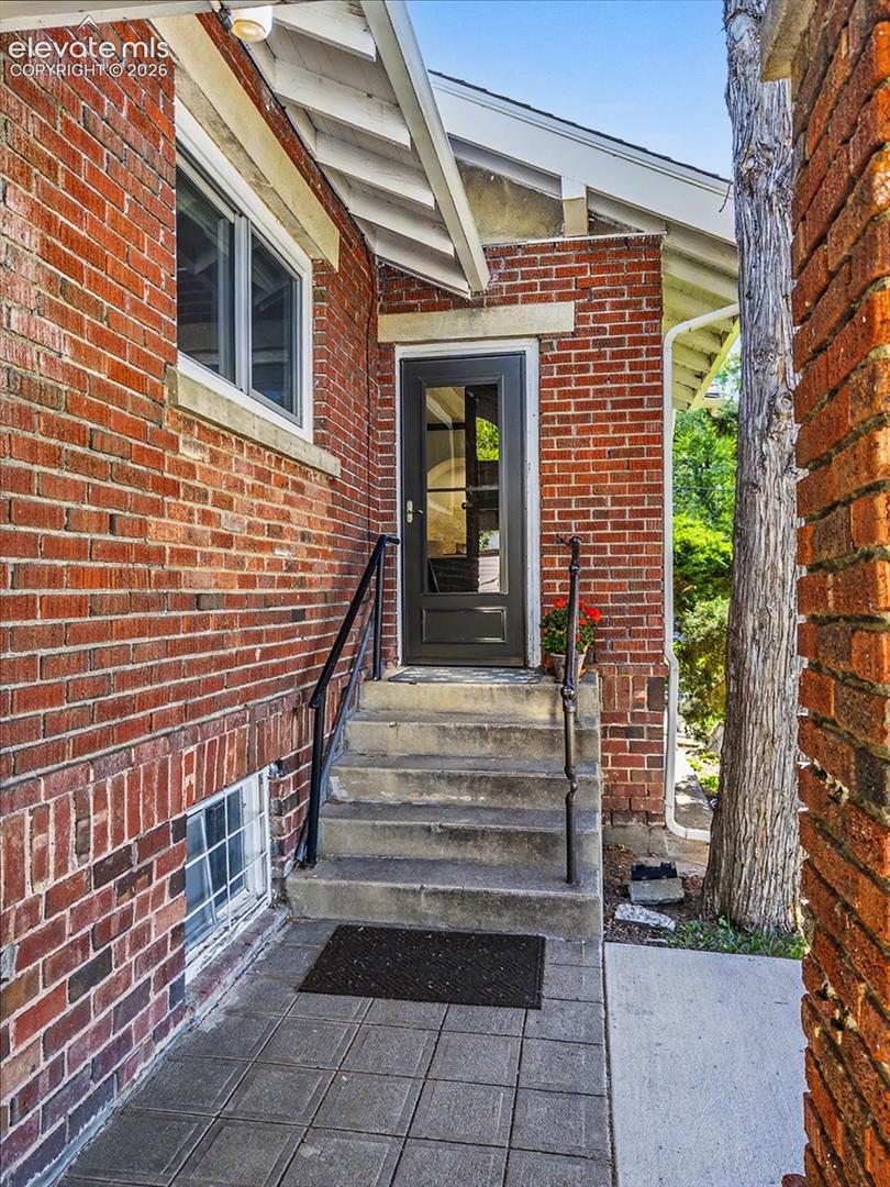 Brick exterior with a walk-out kitchen covered entry on side of home concrete steps, and a dark-paneled door with glass inserts