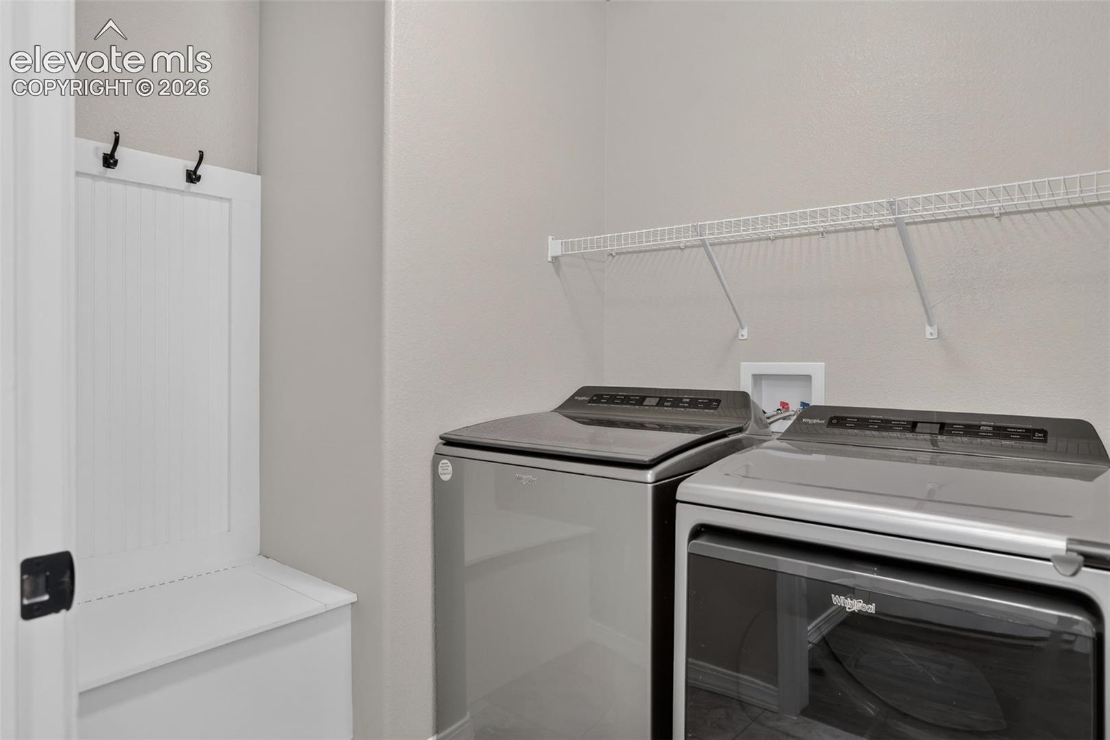 Built-in storage bench with coat hooks, wire shelving, and light gray walls