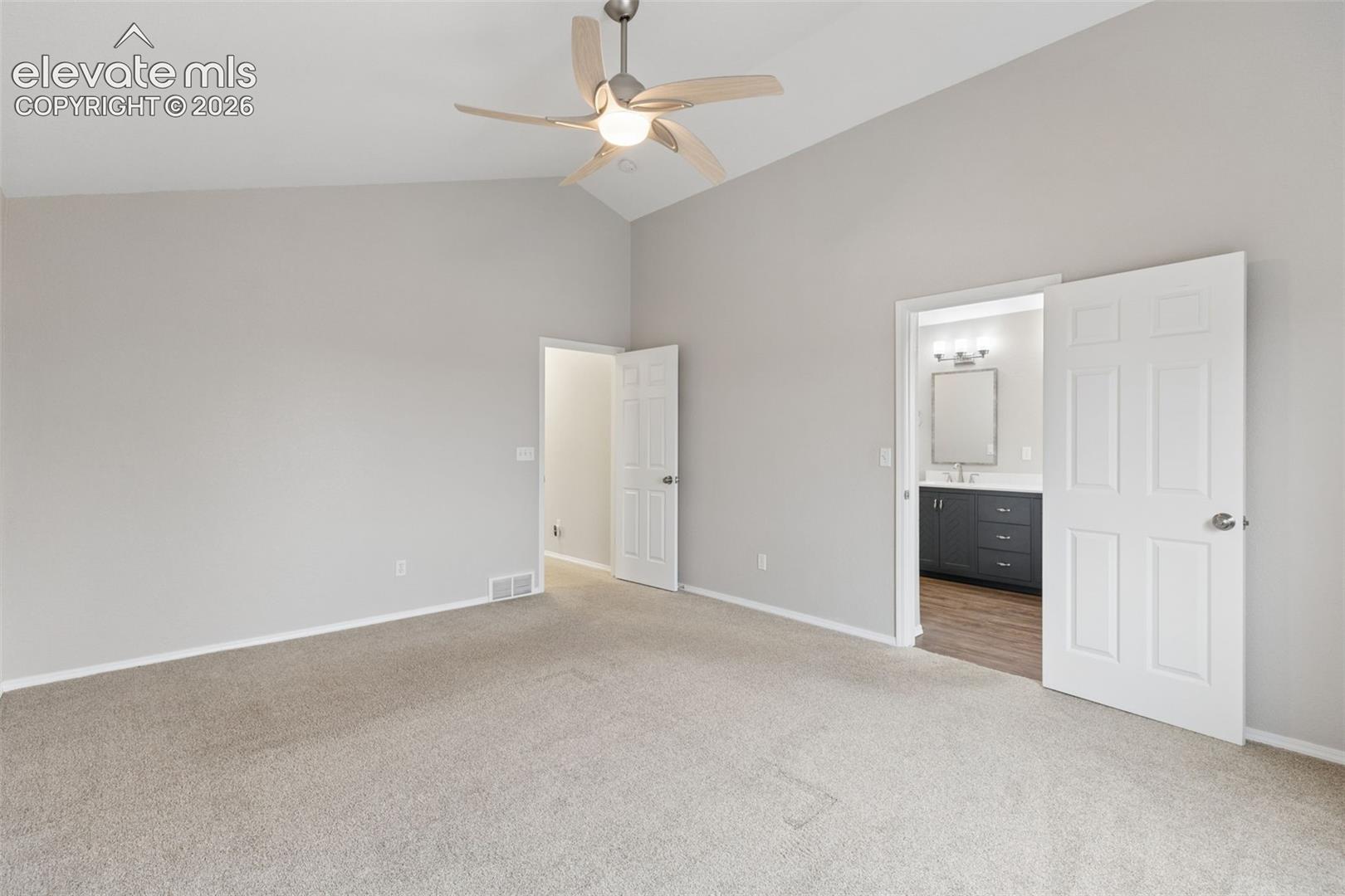 Vaulted ceilings featuring a central ceiling fan, neutral wall paint, carpeted flooring, and multi-panel interior doors
