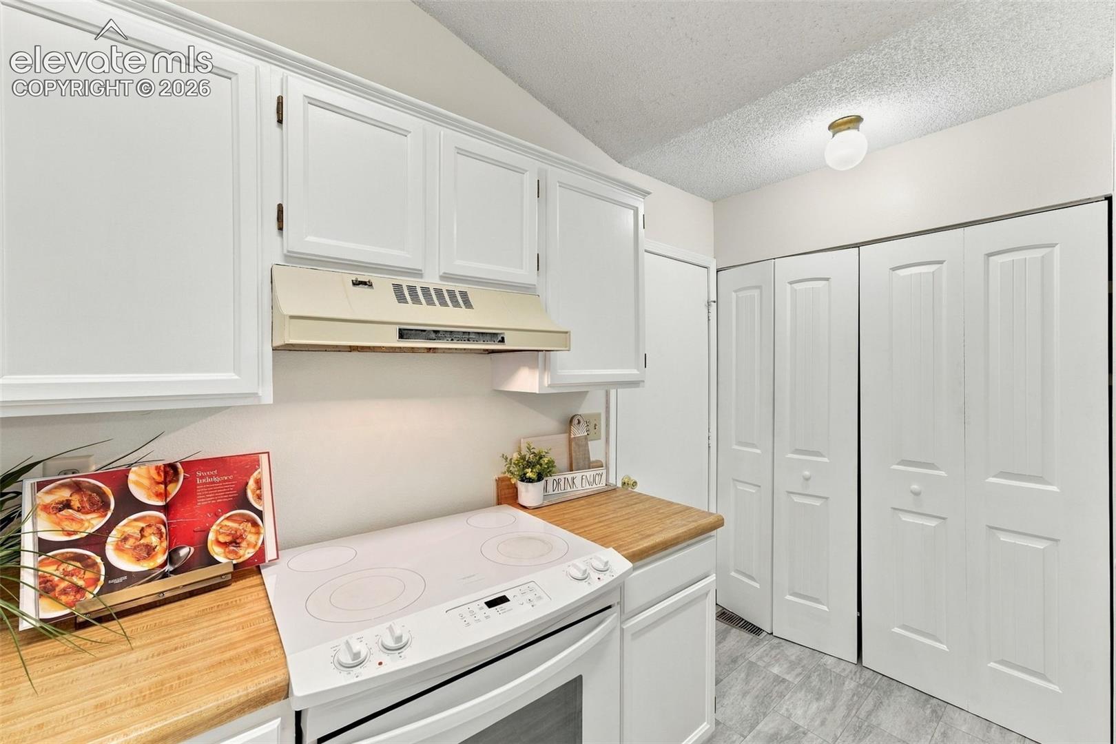 Kitchen featuring white cabinetry, wood-finish countertops, an integrated white range, and floor-to-ceiling bi-fold closet doors