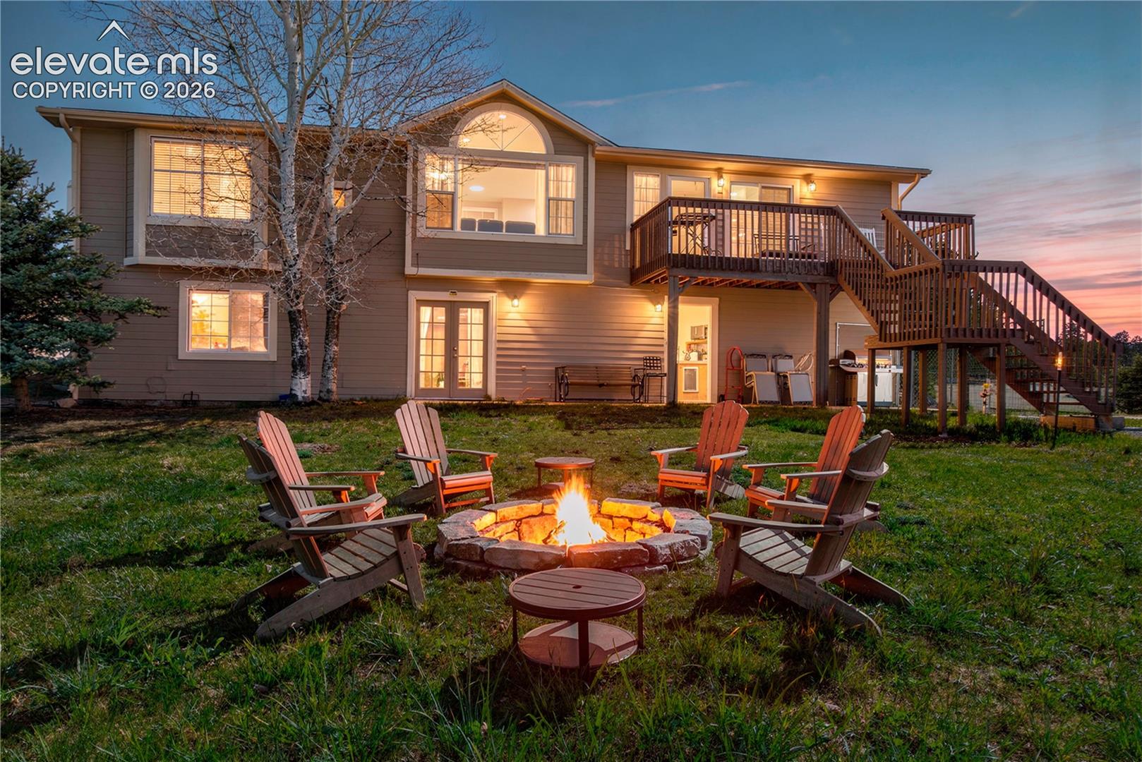 Rear elevation featuring a multi-level wood deck, an arched window, virtual fire pit, and double-door access