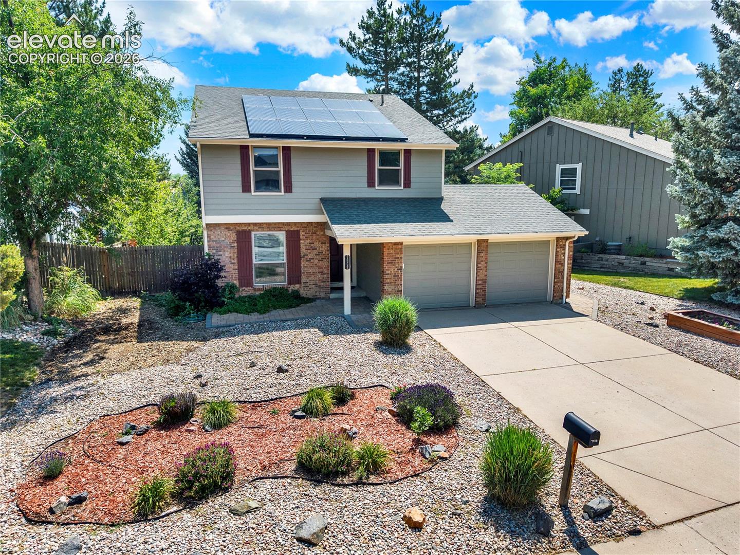 Two-story exterior featuring a brick and siding facade, solar panels, a two-car garage, and xeriscaped front grounds
