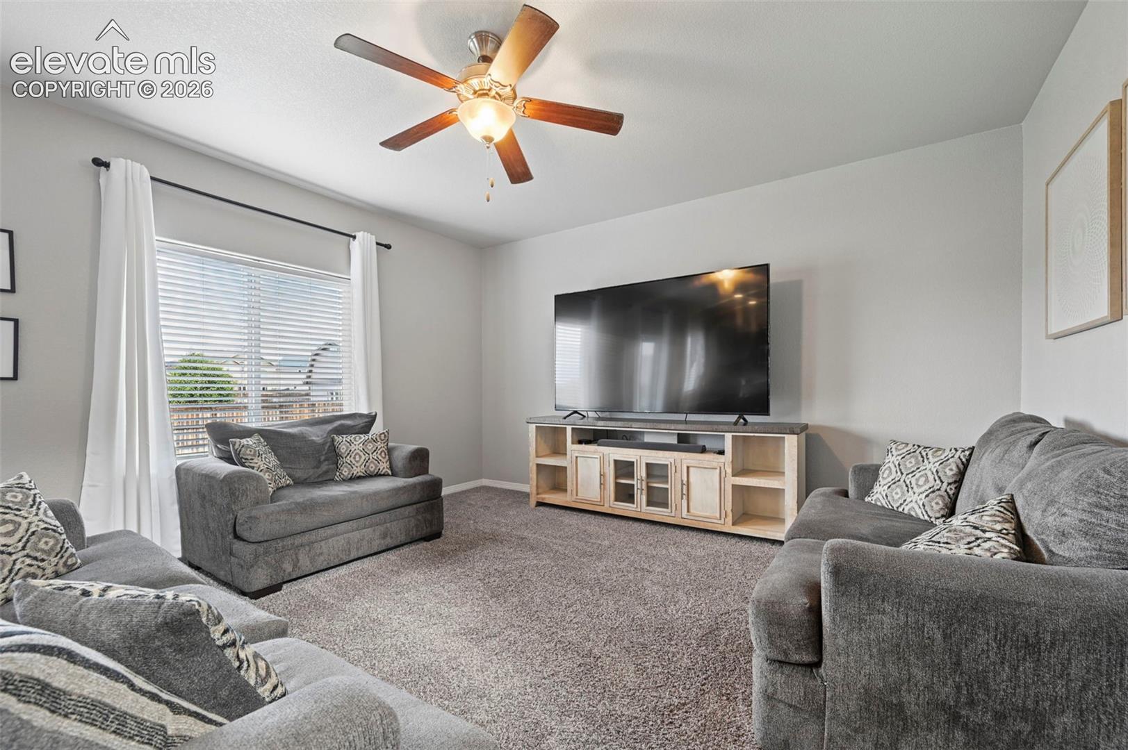 Textured carpet flooring, ceiling fan with integrated lighting, window with blinds, and light-toned walls
