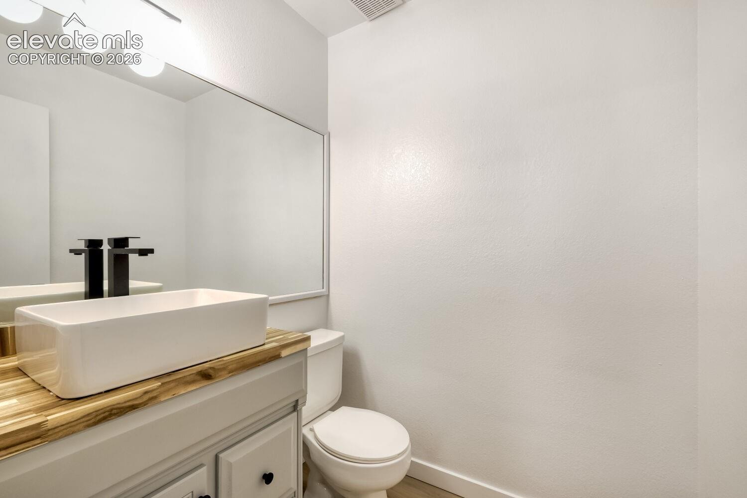 Bathroom featuring a vanity with a light wood-tone countertop, rectangular vessel sink, matte black faucet, full-width mirror, and attached multi-bulb light fixture