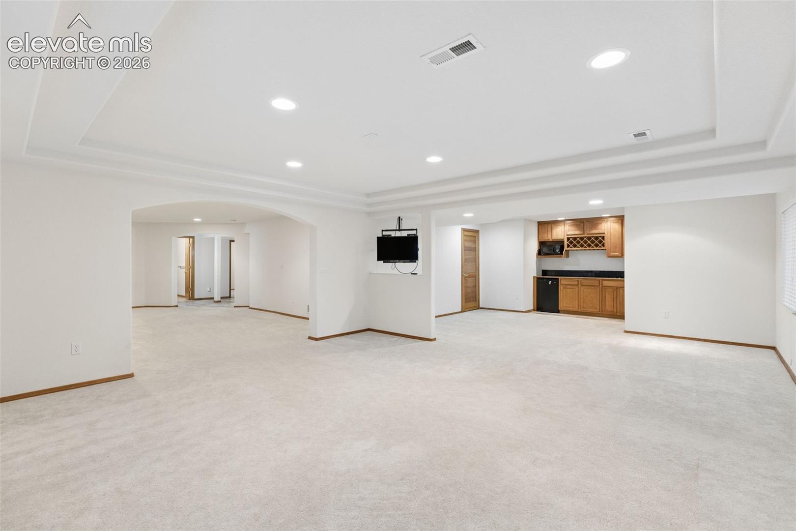 Tray ceiling, recessed lighting, arched entryways, and a wet bar featuring wooden cabinetry and built-in wine rack