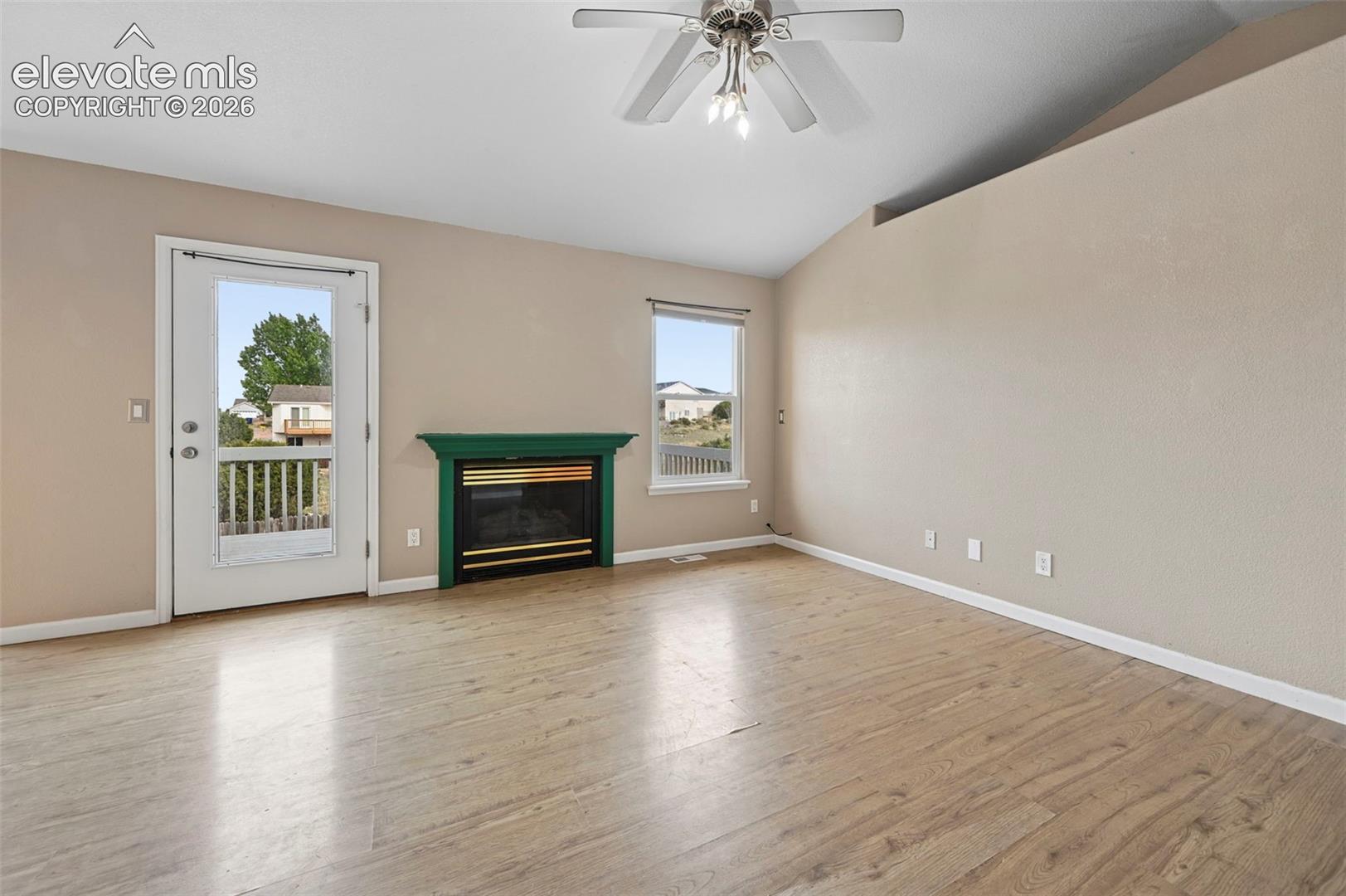Spacious room featuring light wood-finish flooring, a decorative fireplace with a green mantel, and a ceiling fan with integrated lighting