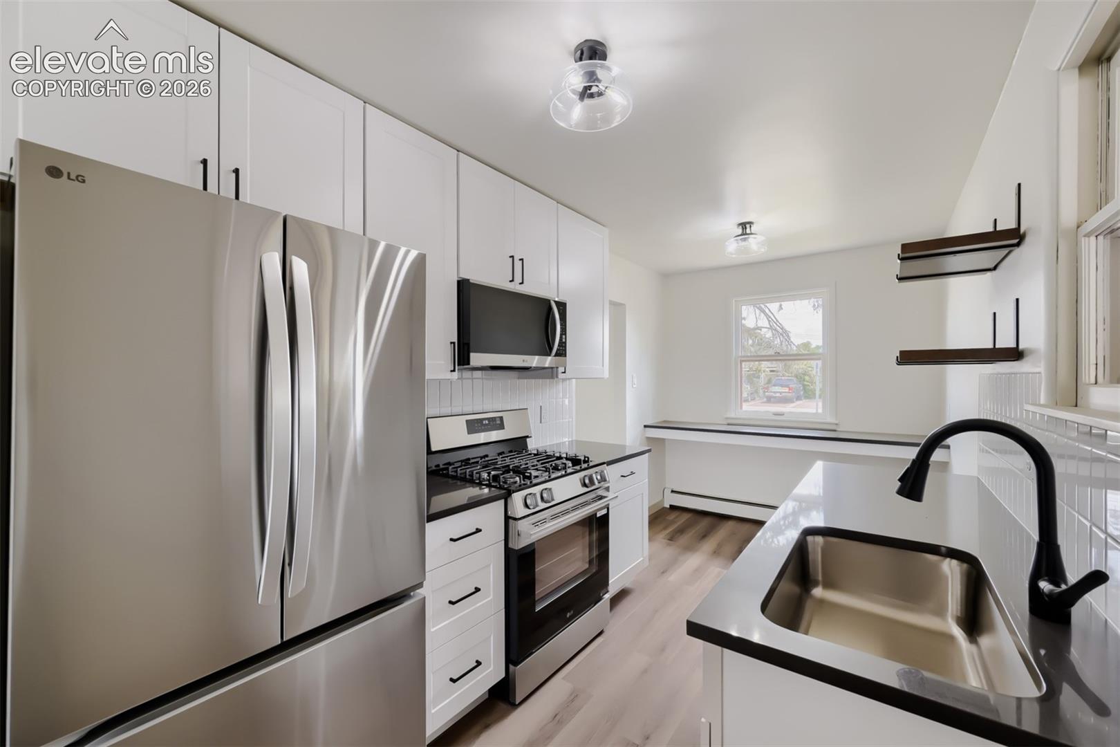 Stainless steel appliances, white shaker cabinetry, dark countertops, a stainless steel sink with a matte black faucet, and wood-finish flooring