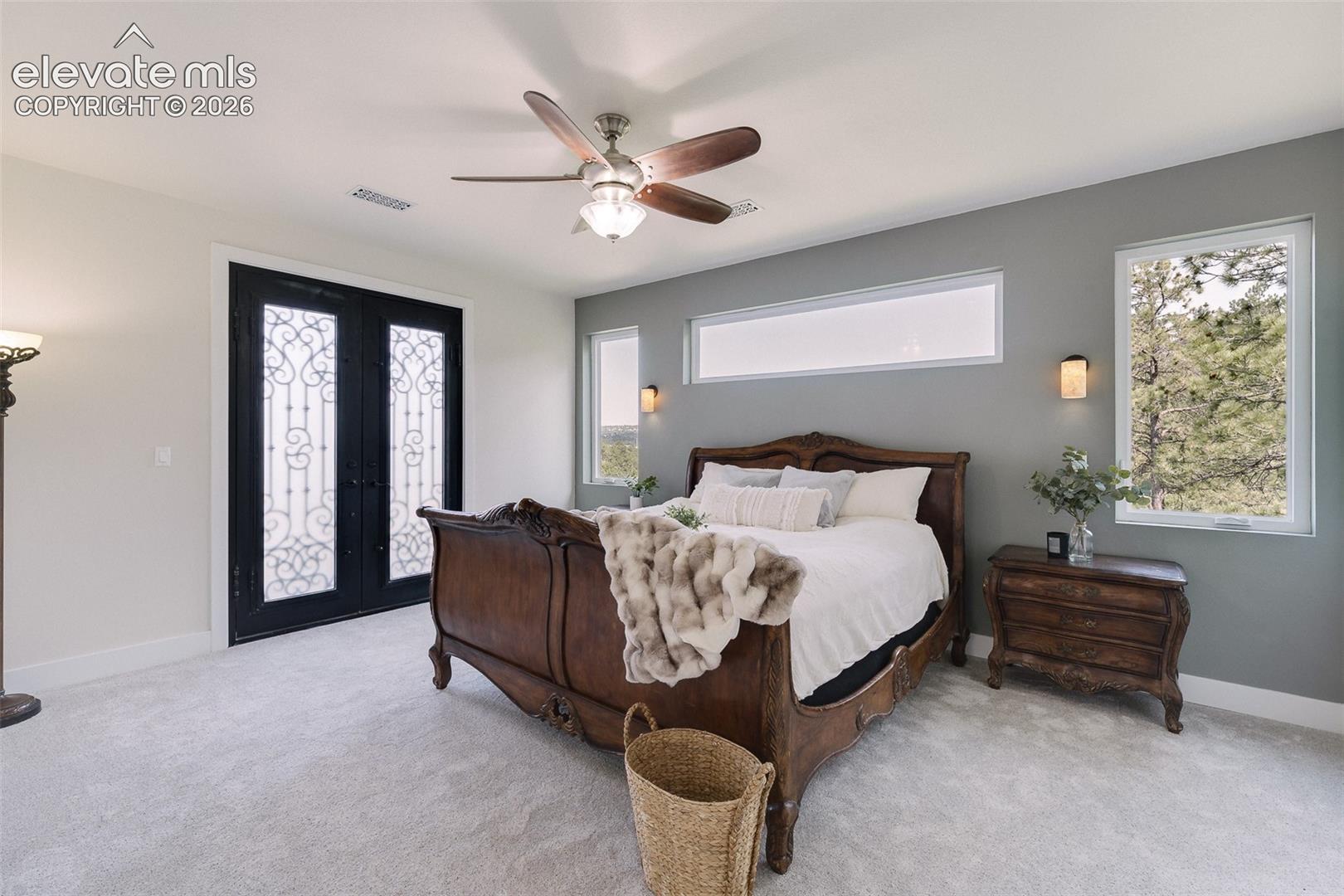 Upper Level Primary Retreat with neutral carpet, a lighted ceiling fan, and gorgeous wood and iron French doors out to a private balcony.