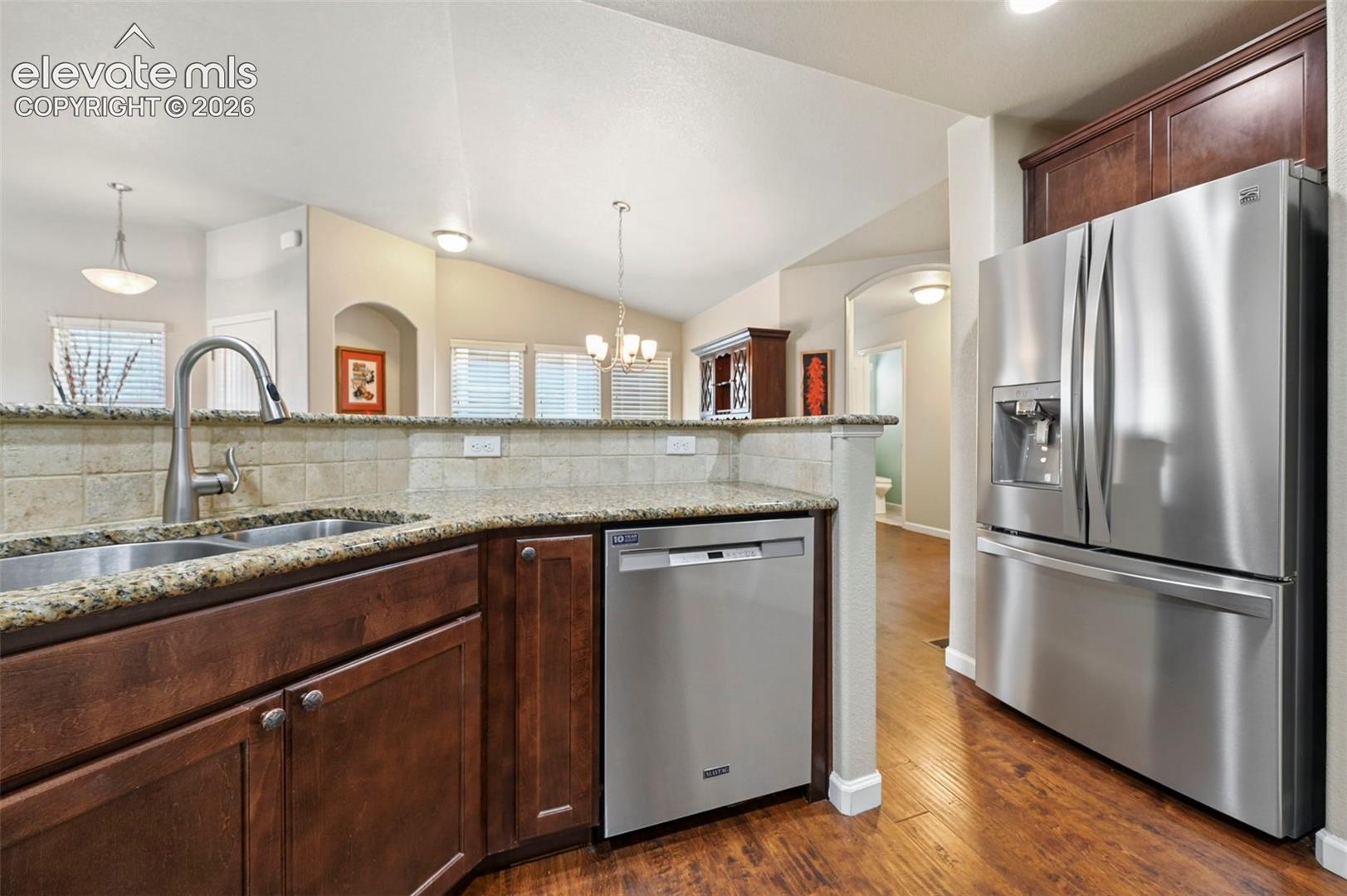Kitchen featuring stainless steel appliances,dark wood cabinetry, a double basin sink with a gooseneck faucet, convenient pull-out trash cabinet